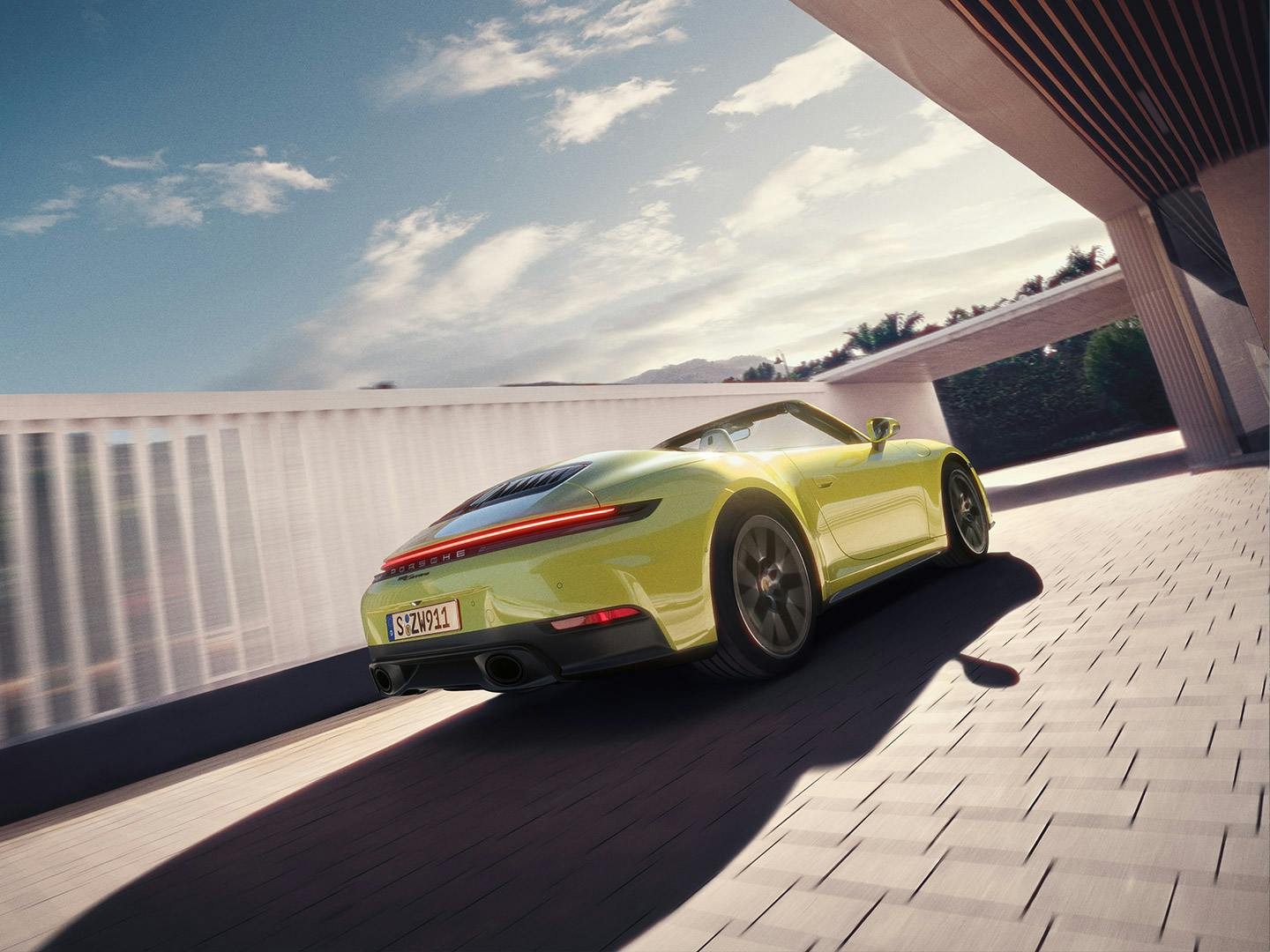 A yellow Porsche 911 Cabriolet driving out of a driveway of a modern building.