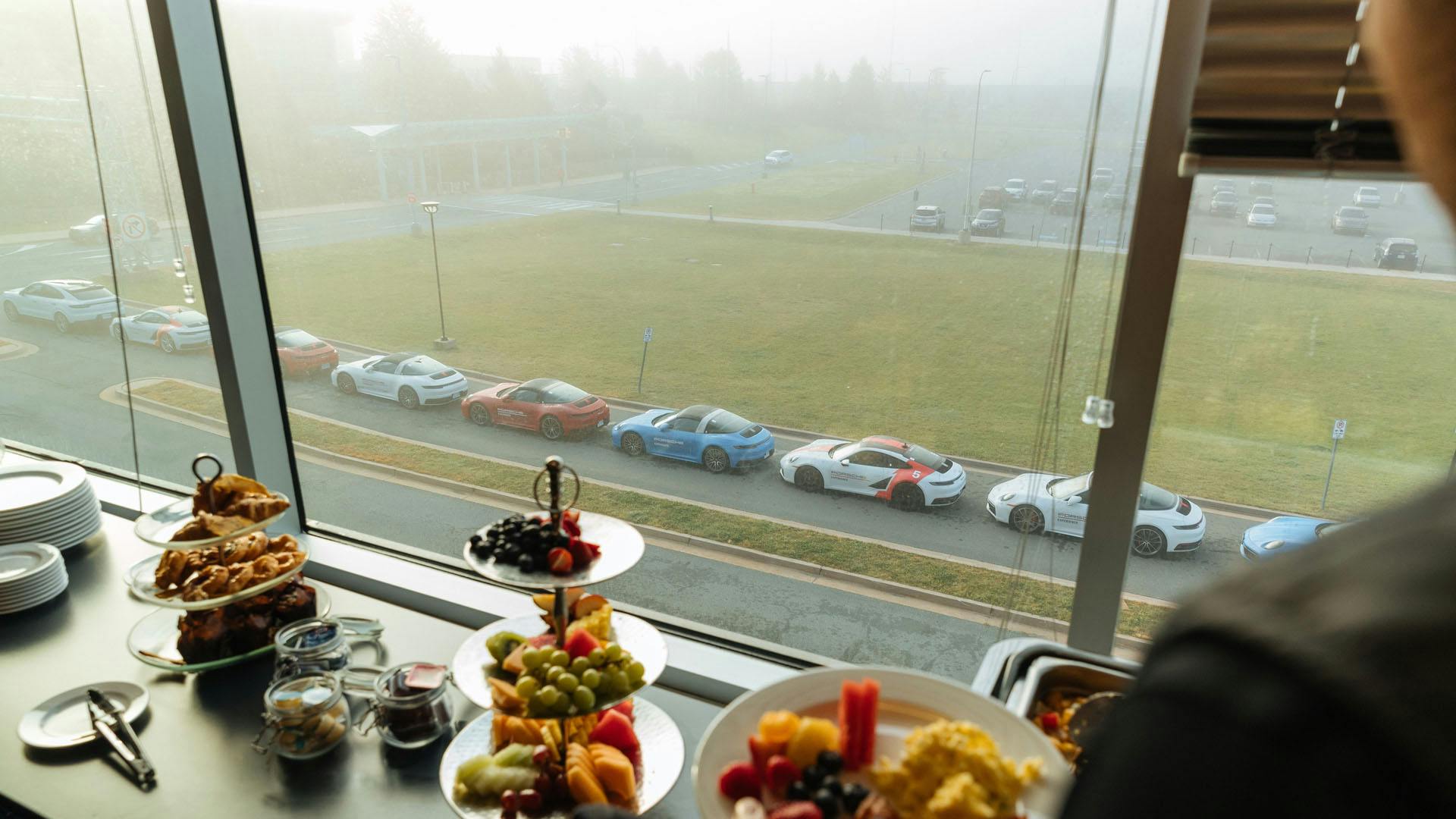 Vue de l'intérieur d'un restaurant avec un groupe de Porsche 911 stationnées dans la rue.