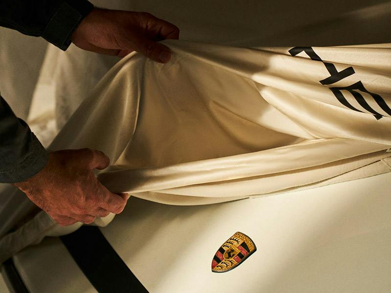 Two hands removing a protection cover from a Porsche Classic car.