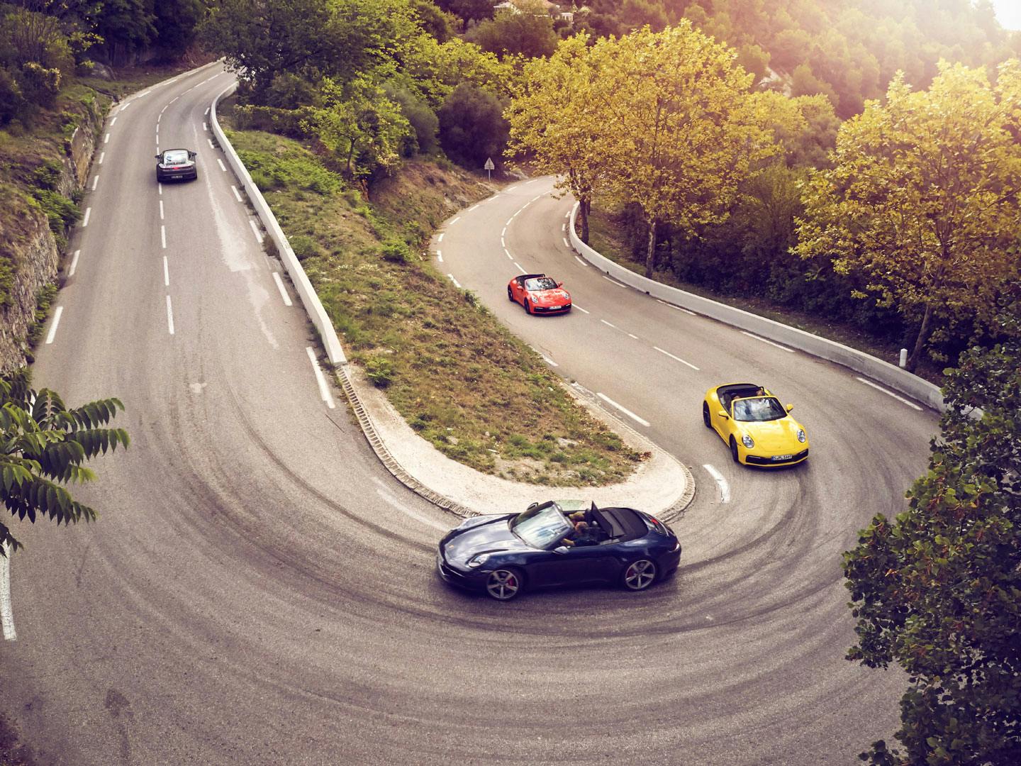 Flera Porsche-bilar åker tillsammans på en väg uppför en krokig backe.