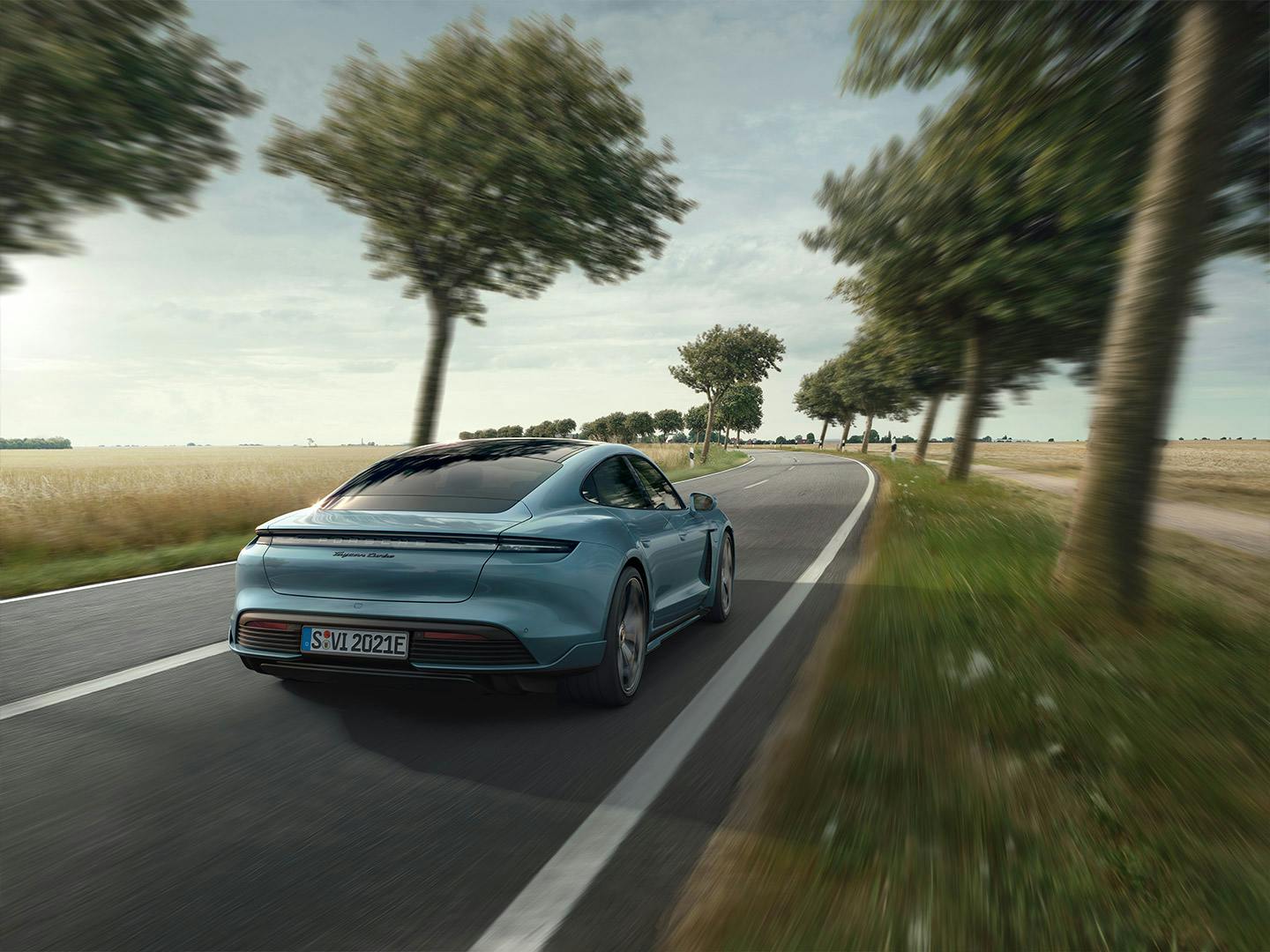 A Porsche Taycan Turbo in blue on a road in the countryside.