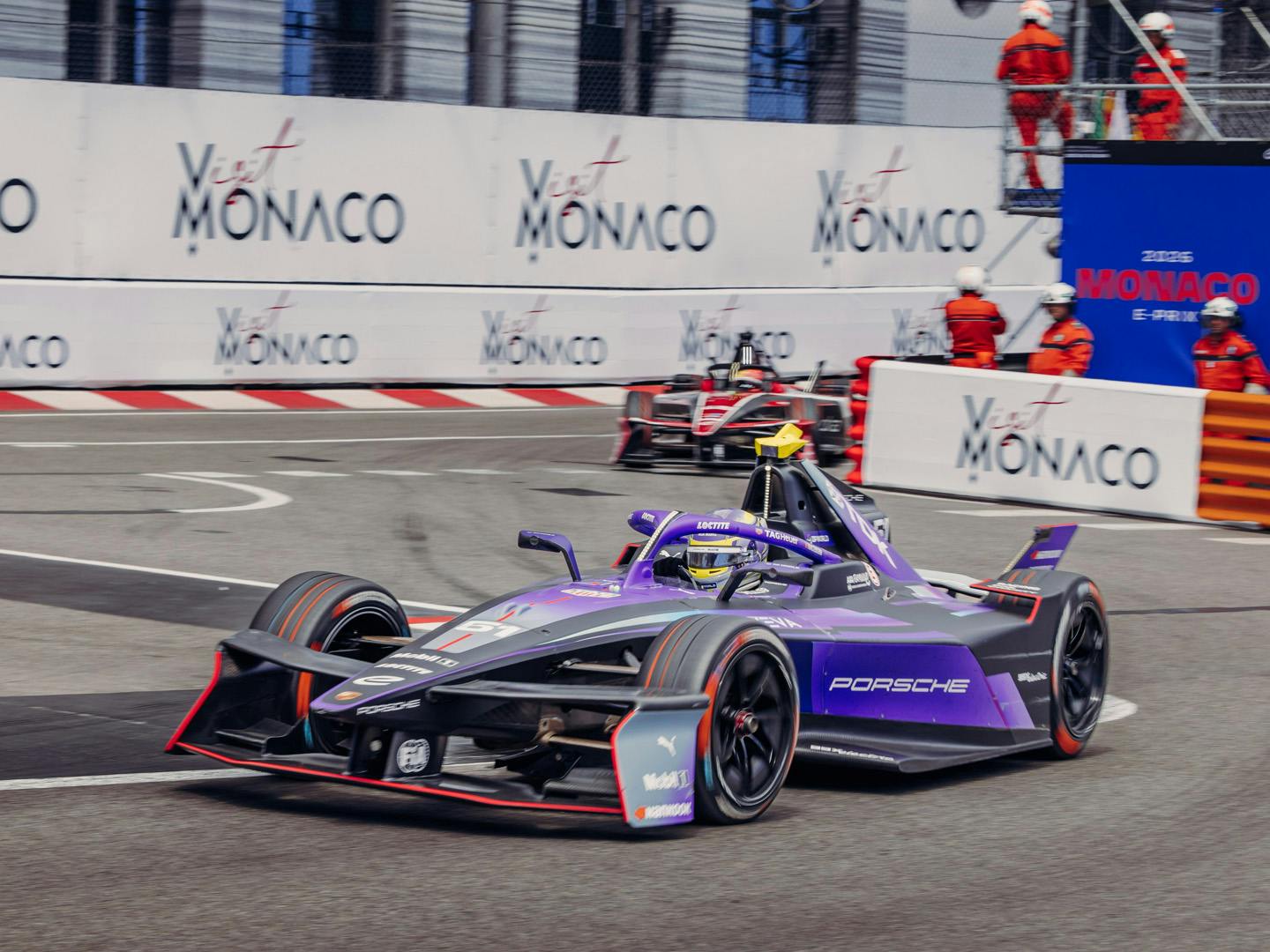 The purple and black Porsche 99X Electric Formula E single‑seater racing through the streets of Monaco, with a second car following behind.