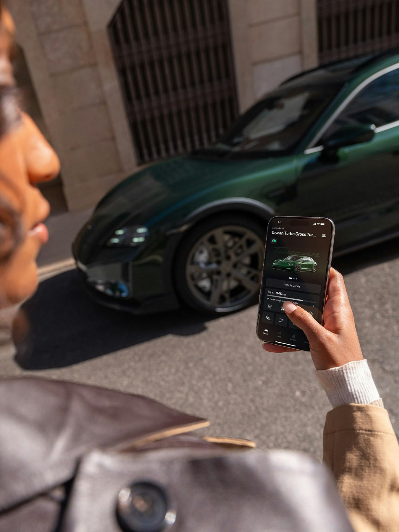 A woman using the My Porsche app while a Porsche Taycan can be seen in the background.