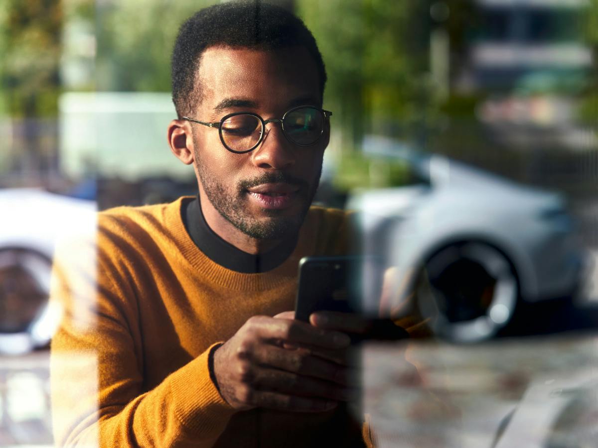 Un jeune homme regarde son téléphone portable. On peut voir une Porsche en arrière-plan.