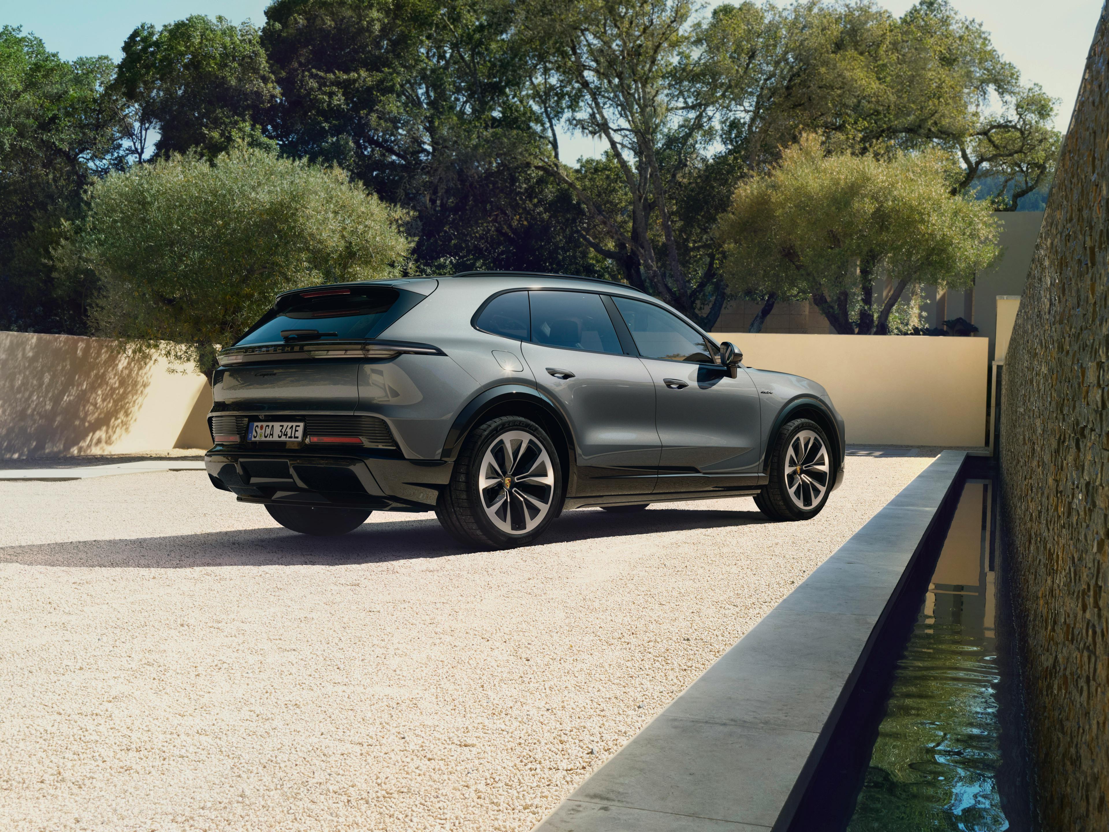 The Cayenne Electric SUV parked on a light coloured pebble ground while facing the wall, there are trees in the background.