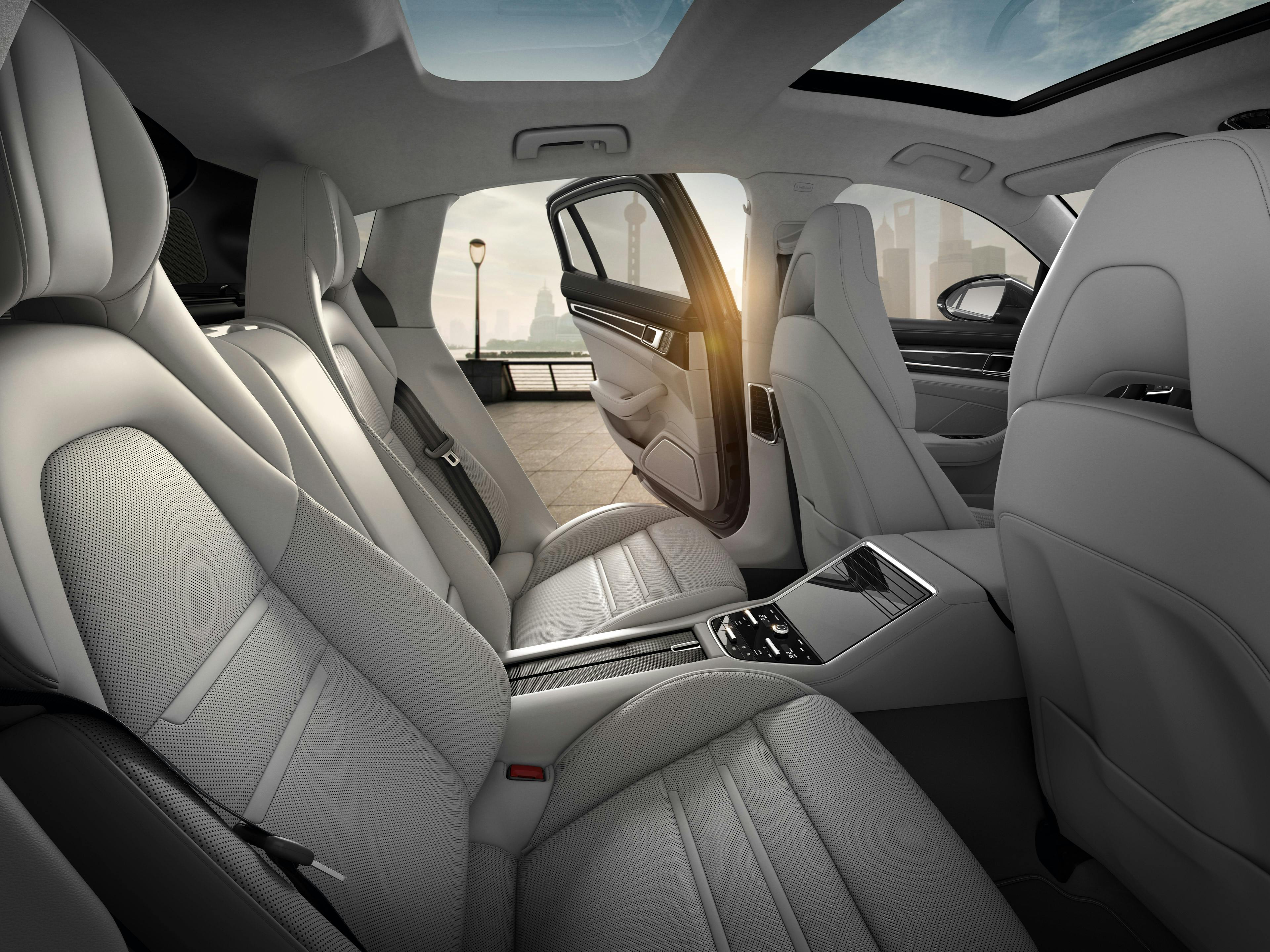 Die hintere Sitzreihe eines Porsche mit weißen Ledersitzen, einem Panoramadach und einer Mittelkonsole mit Touchscreen.