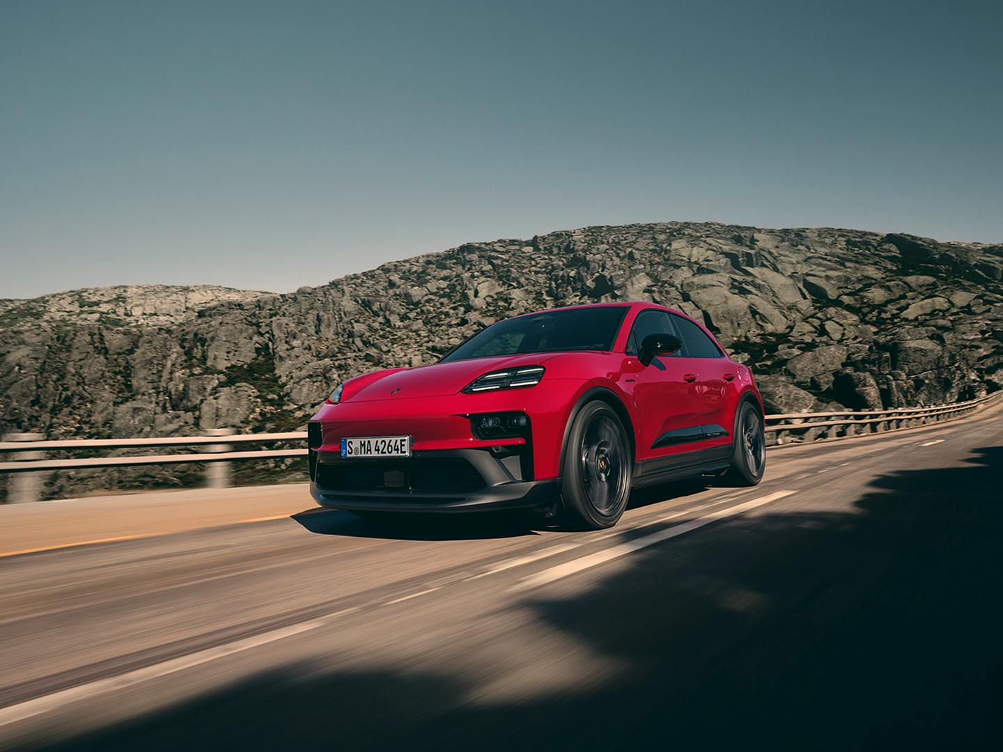 The Macan GTS Electric driving along a road in a mountainous region.