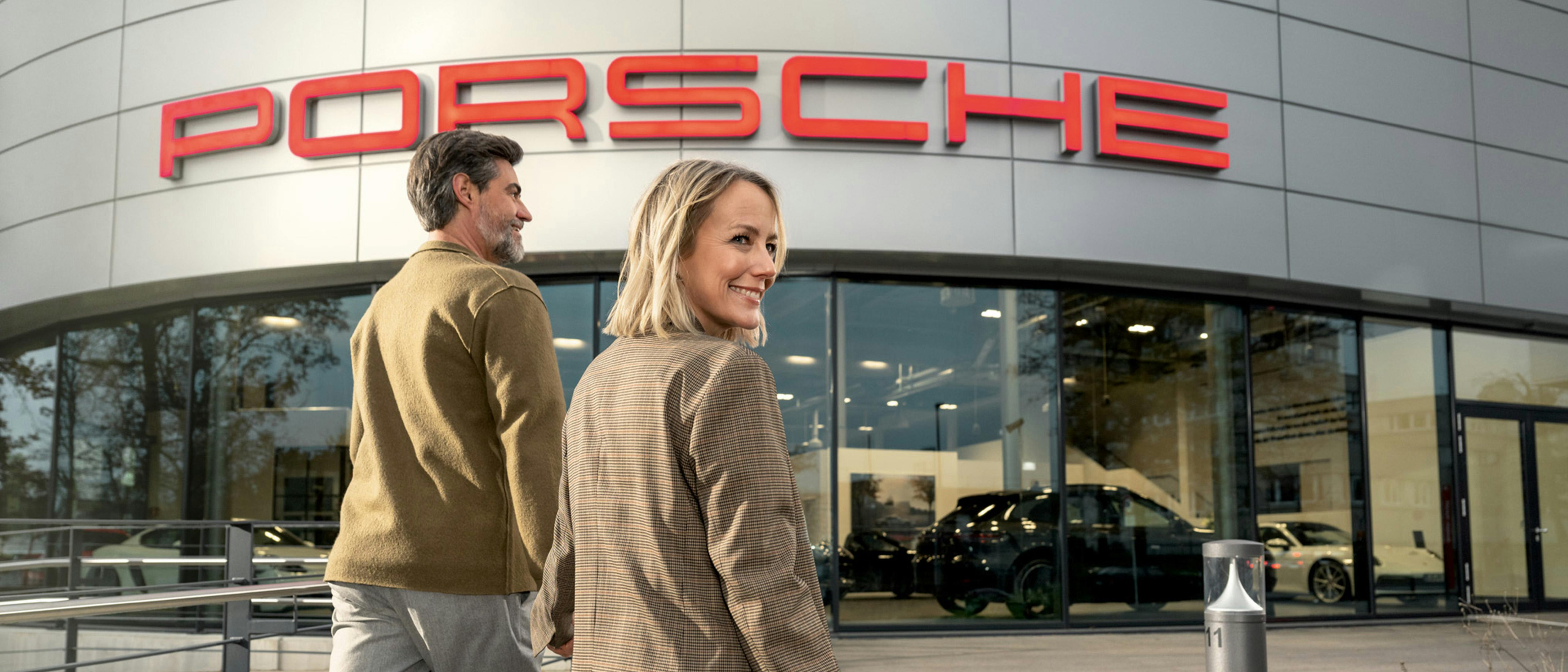 Ein Kundenpaar läuft Hand in Hand zum Eingang des Gebäudes der Porsche Werksabholung.