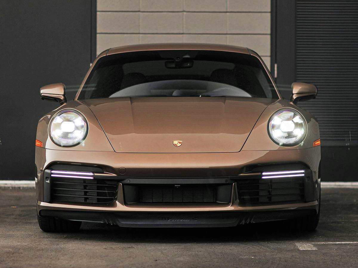 A 911 Turbo S coloured in Copper Brown Metallic from the front in front of a brick building.