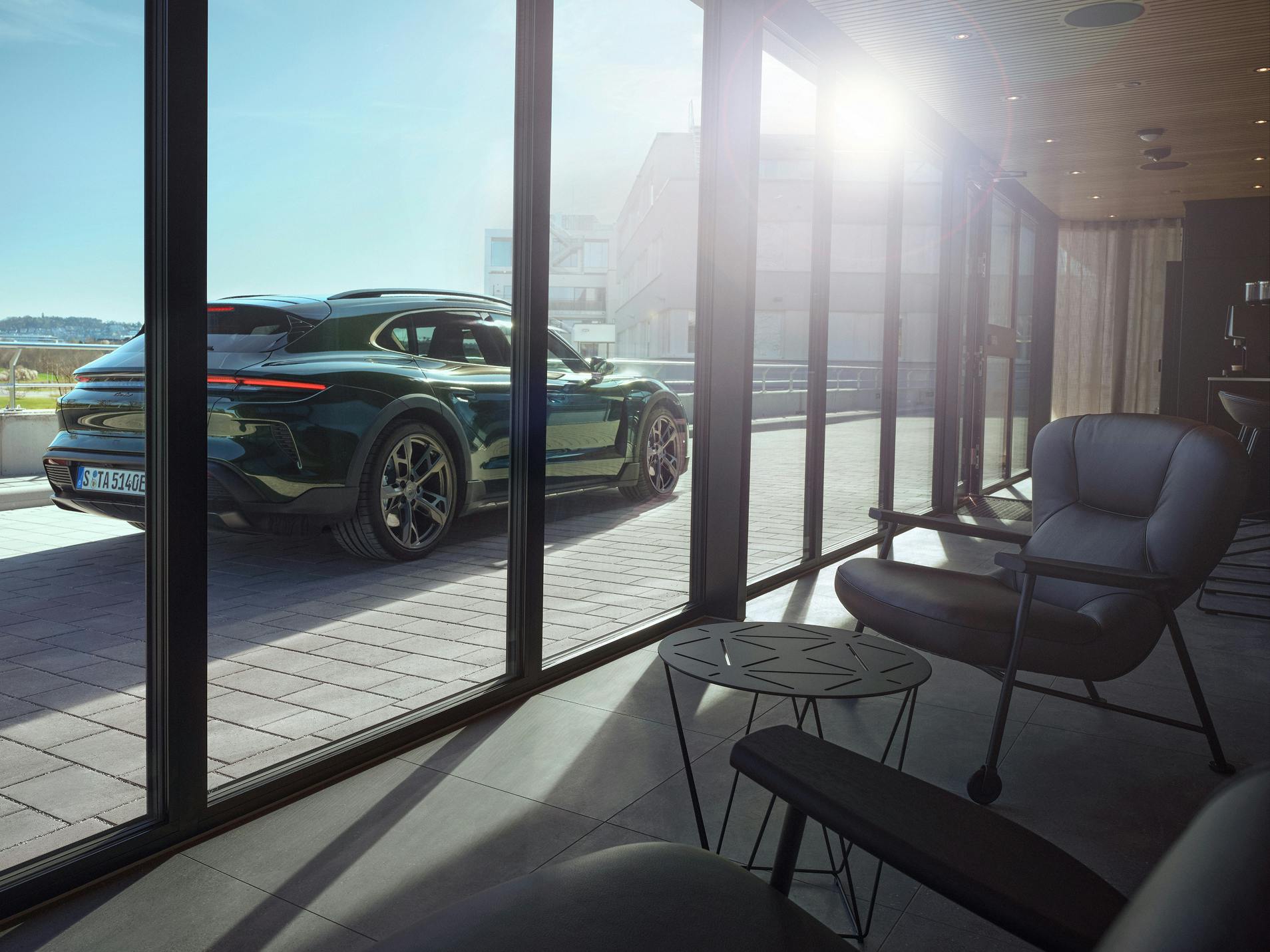 View through the window of a Porsche Charging Lounge to a Porsche Taycan Turbo Cross Turismo parked in front of it.