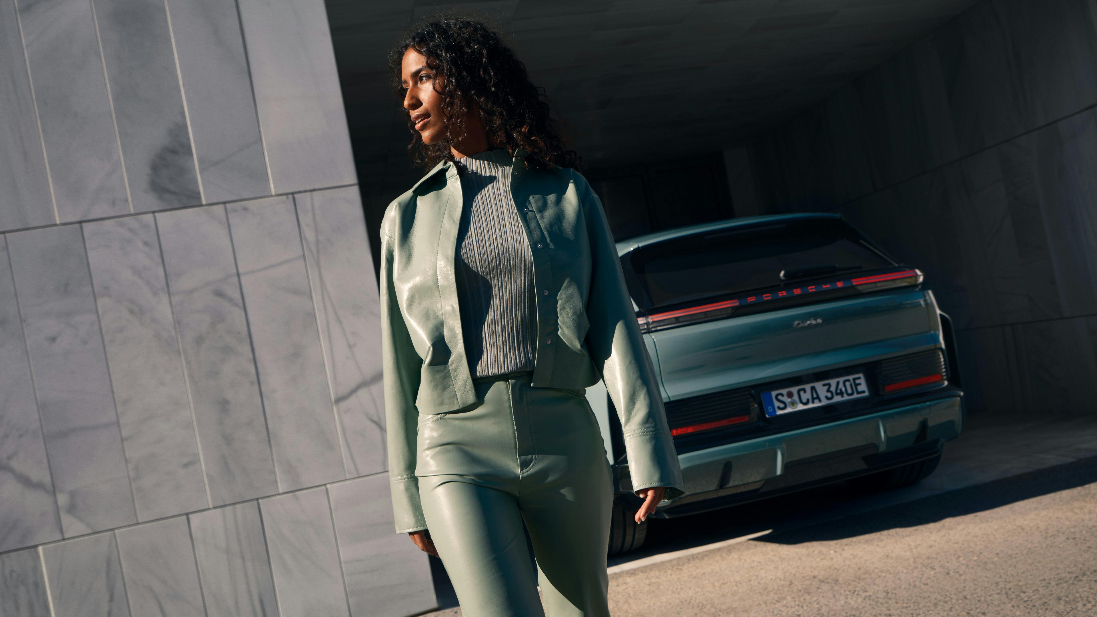 A woman walks past a Porsche Cayenne Turbo, which is seen from behind.
