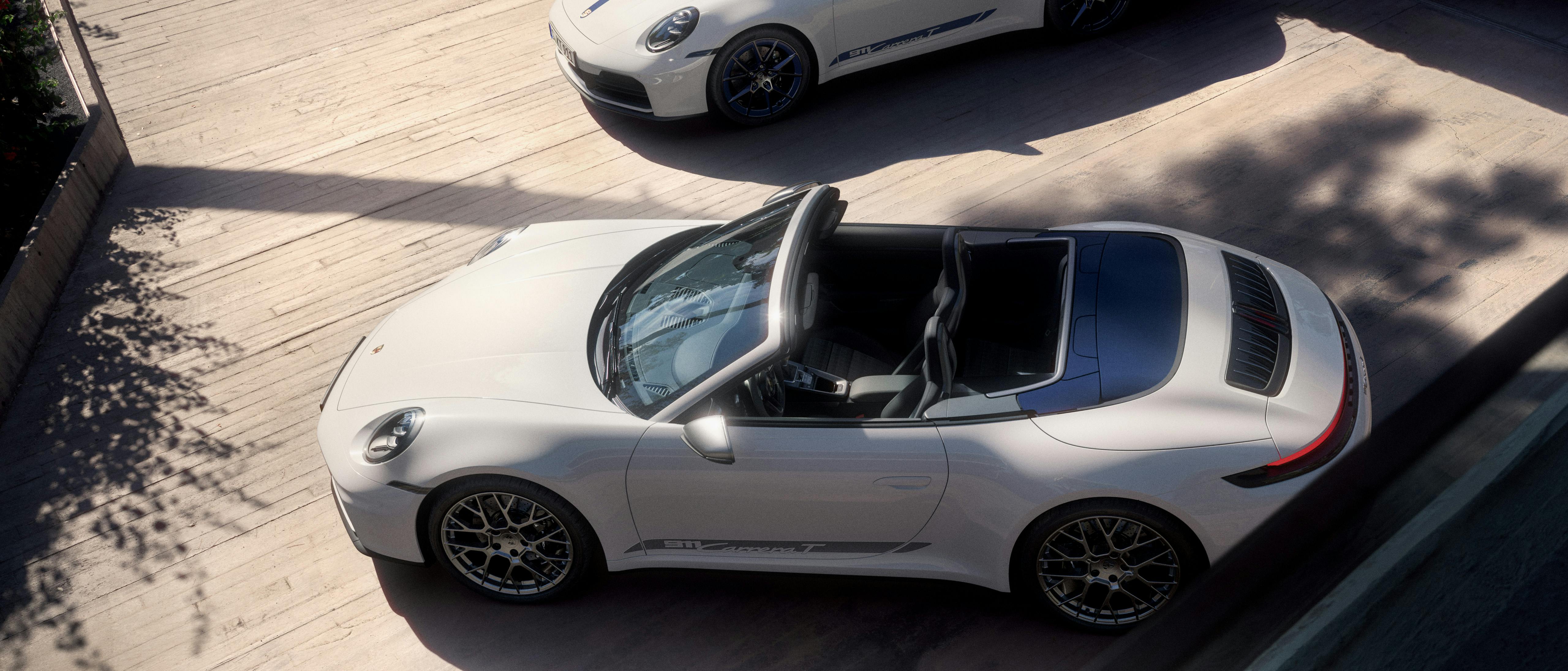 The Porsche 911 Carrera T and Porsche 911 Carrera T Cabriolet, both in white, parked close to each other, with shadows of the periphery over the cars.