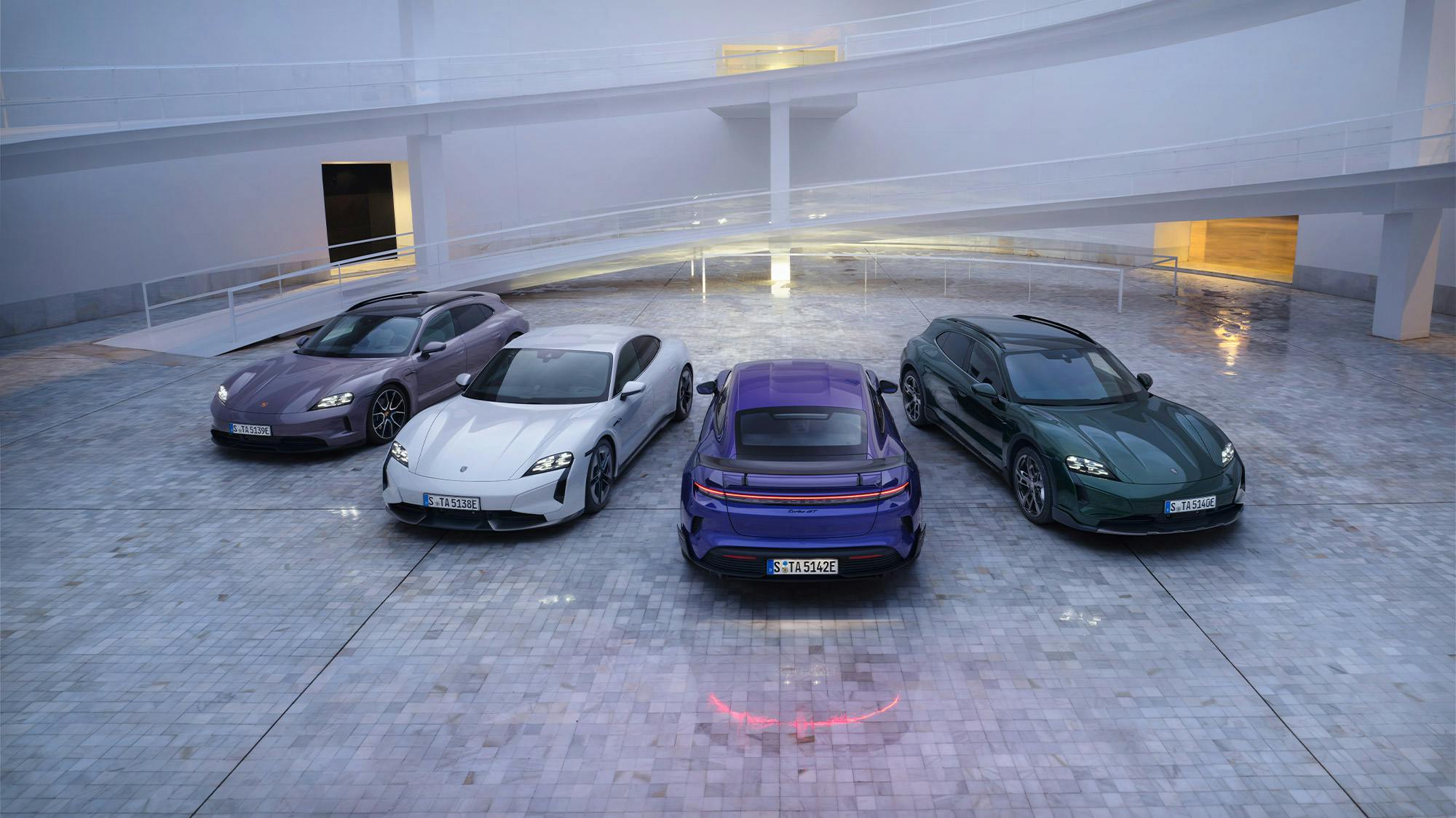 Cuatro modelos diferentes del Porsche Taycan están aparcados a un lado en un atrio.