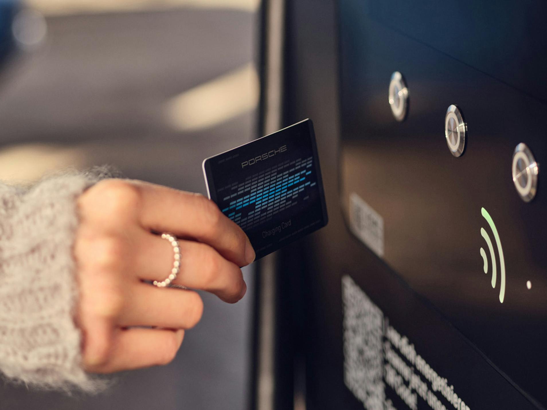 Ręka trzymająca kartę z chipem przed stacją ładowania samochodów elektrycznych.