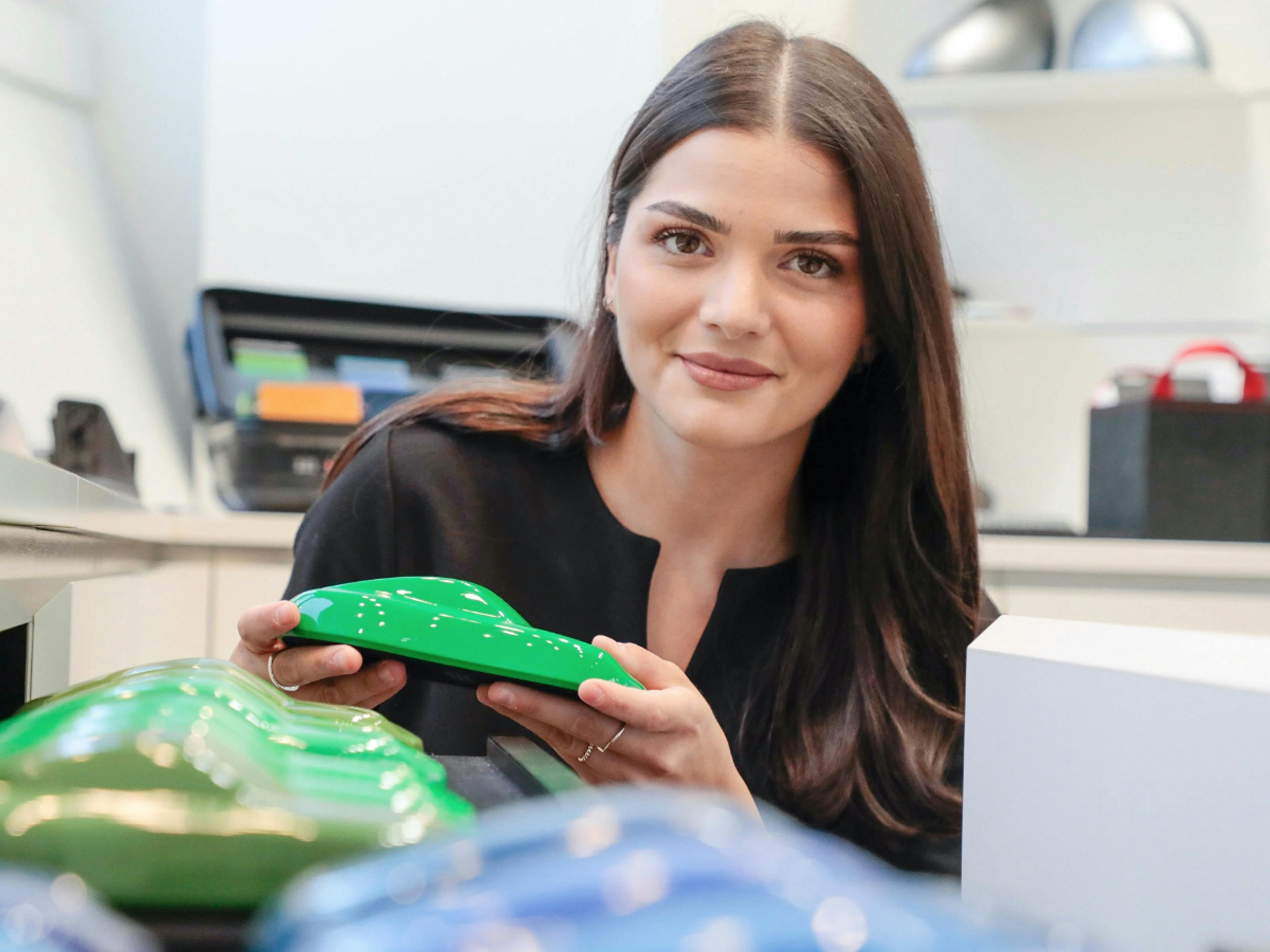 Die Porsche Mitarbeiterin Ebru zeigt ein Modellauto und lächelt in die Kamera.