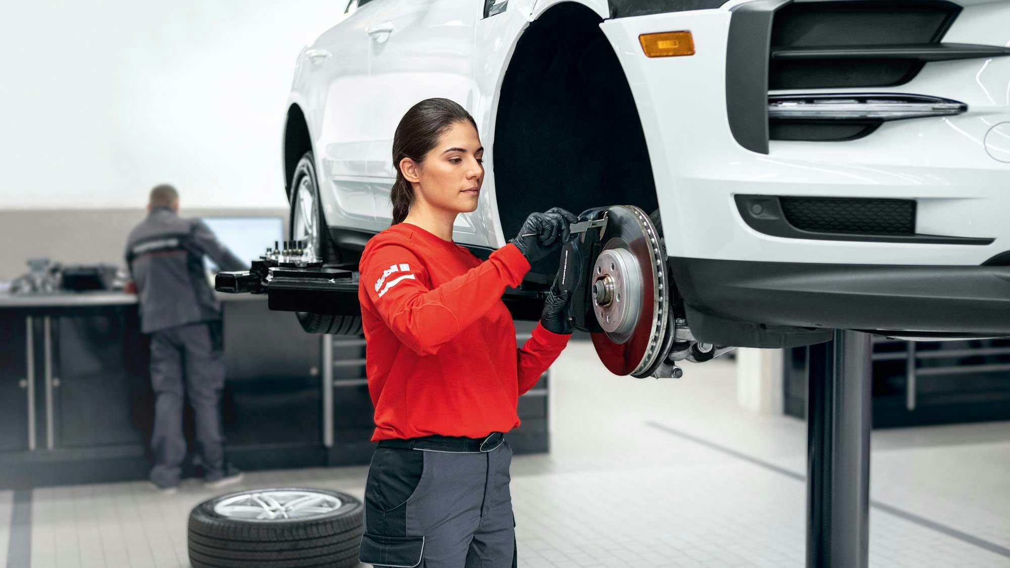 Porsche female mechanic checking the brakes of a vehicle.