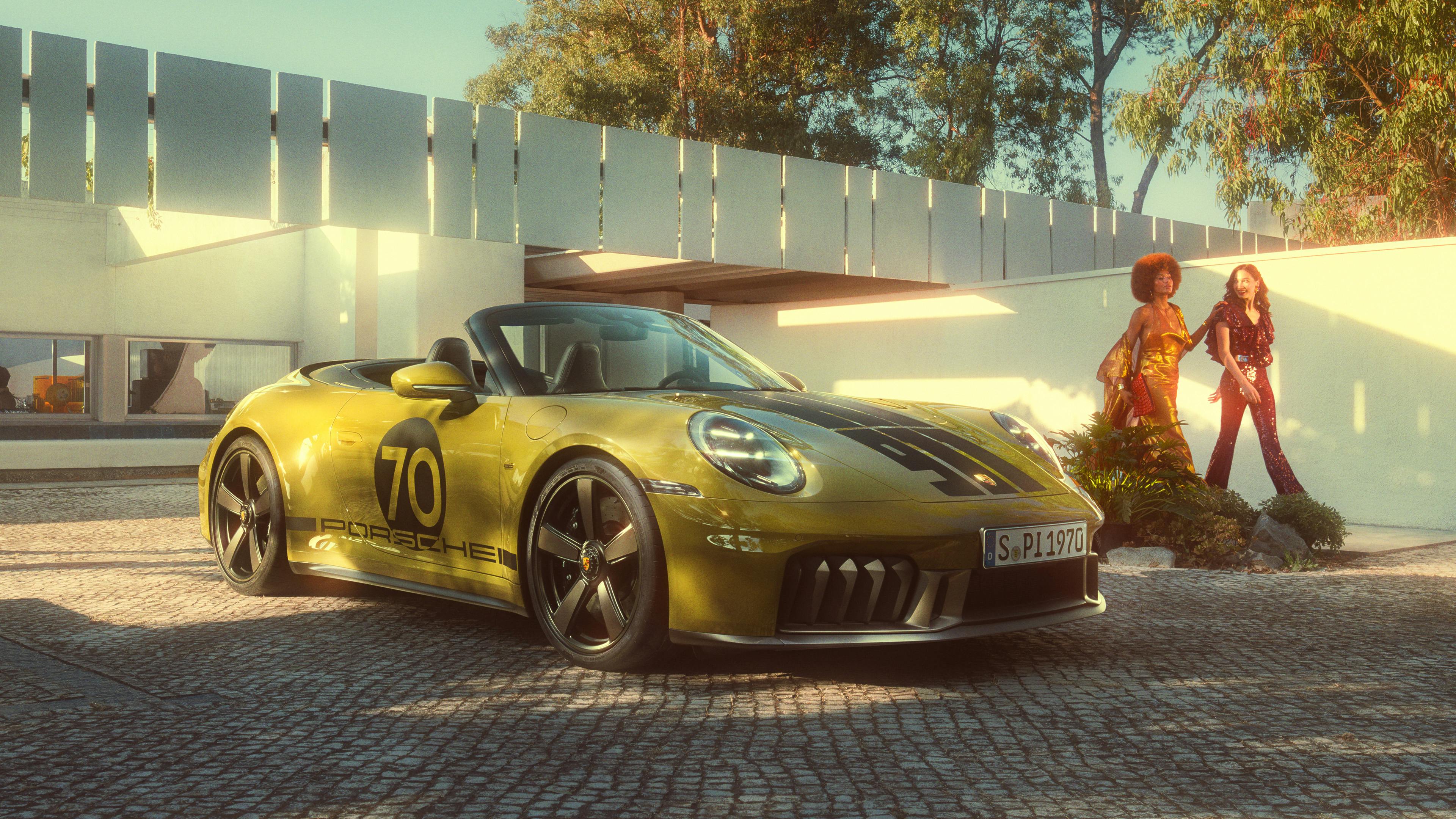 911 Spirit 70 in Olive Neo on a paved square, with two people and modern architecture in the background.