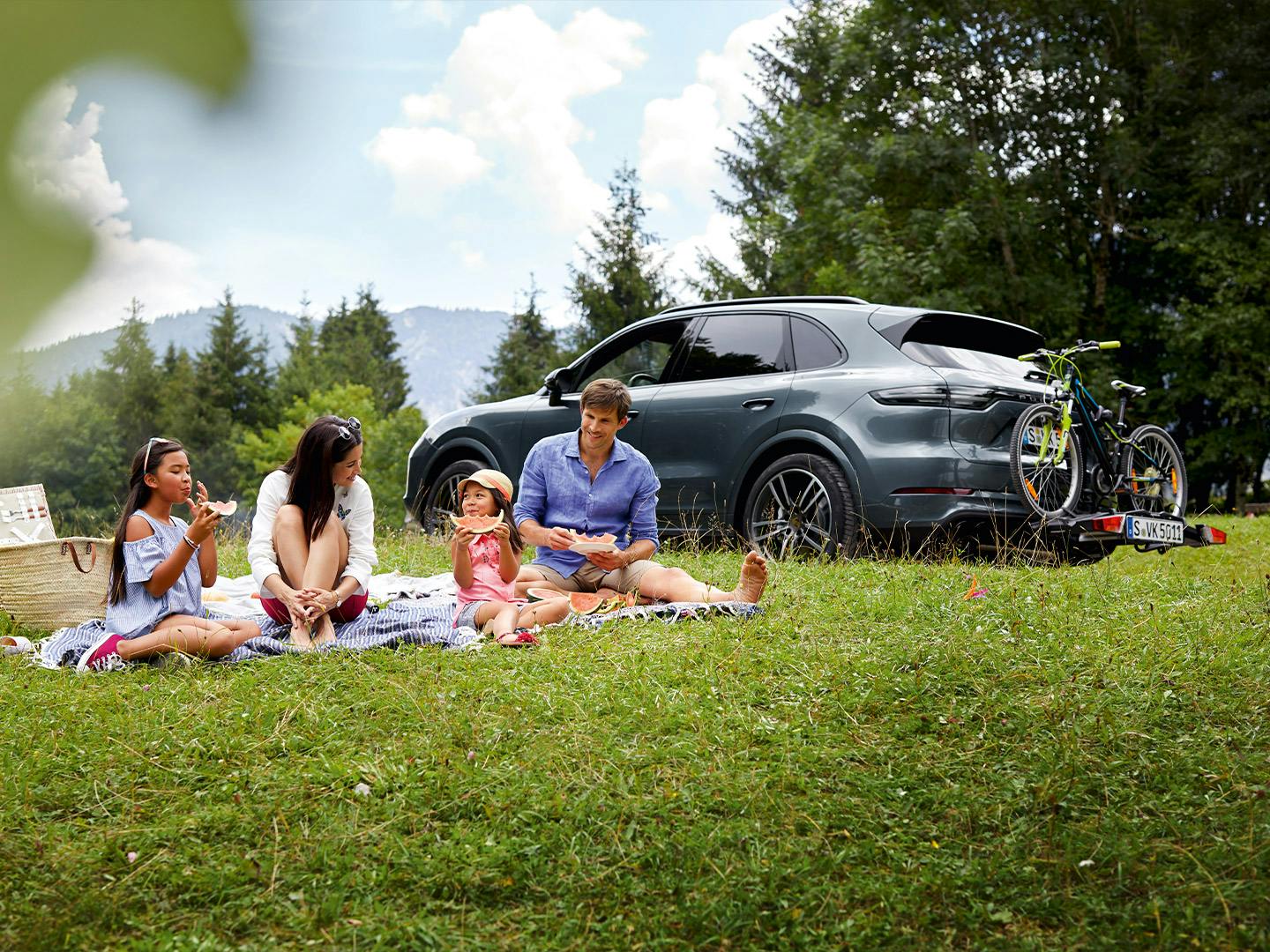 Una familia haciendo un picnic delante de un Porsche Cayenne.