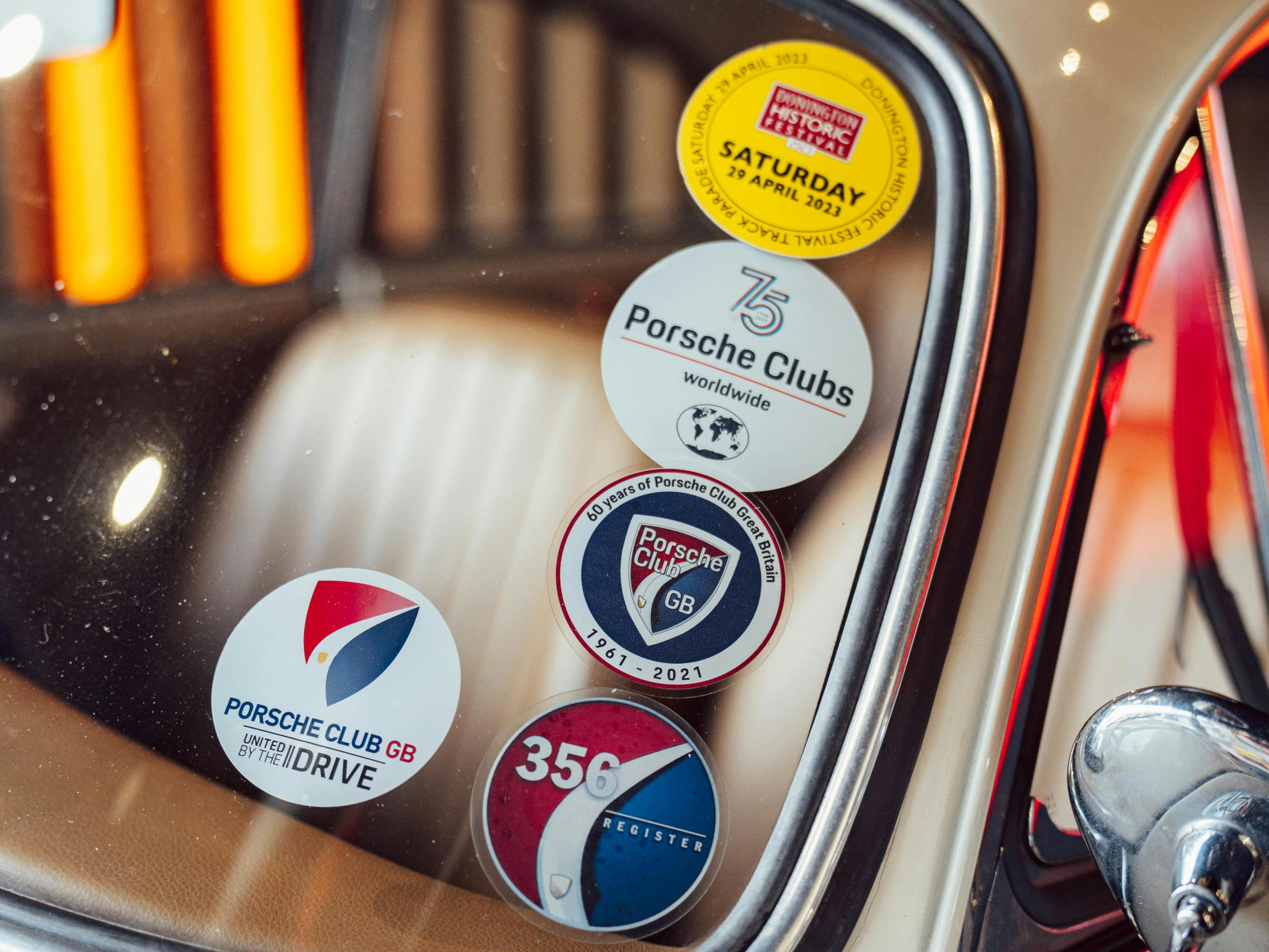 A close-up of the front windshield of a vintage cream coloured Porsche, with several stickers  attached to the glass of the windshield.