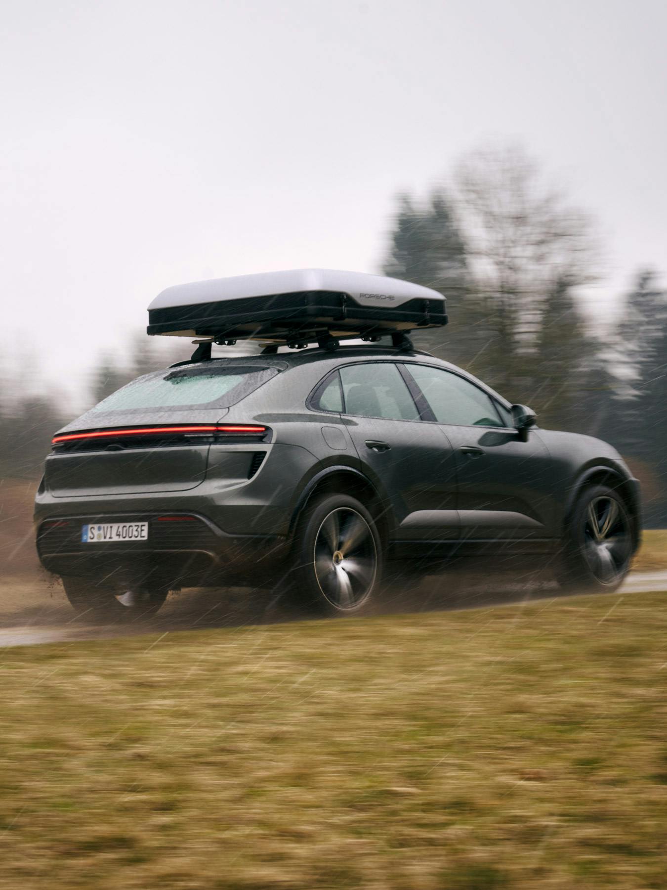 A Porsche Macan with a roof box driving on an unpaved road.