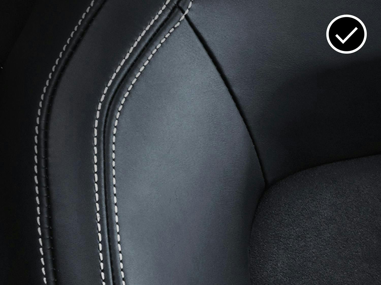 Close-up of a black car seat with smooth, undamaged leather and white stitching, marked with a check symbol.
