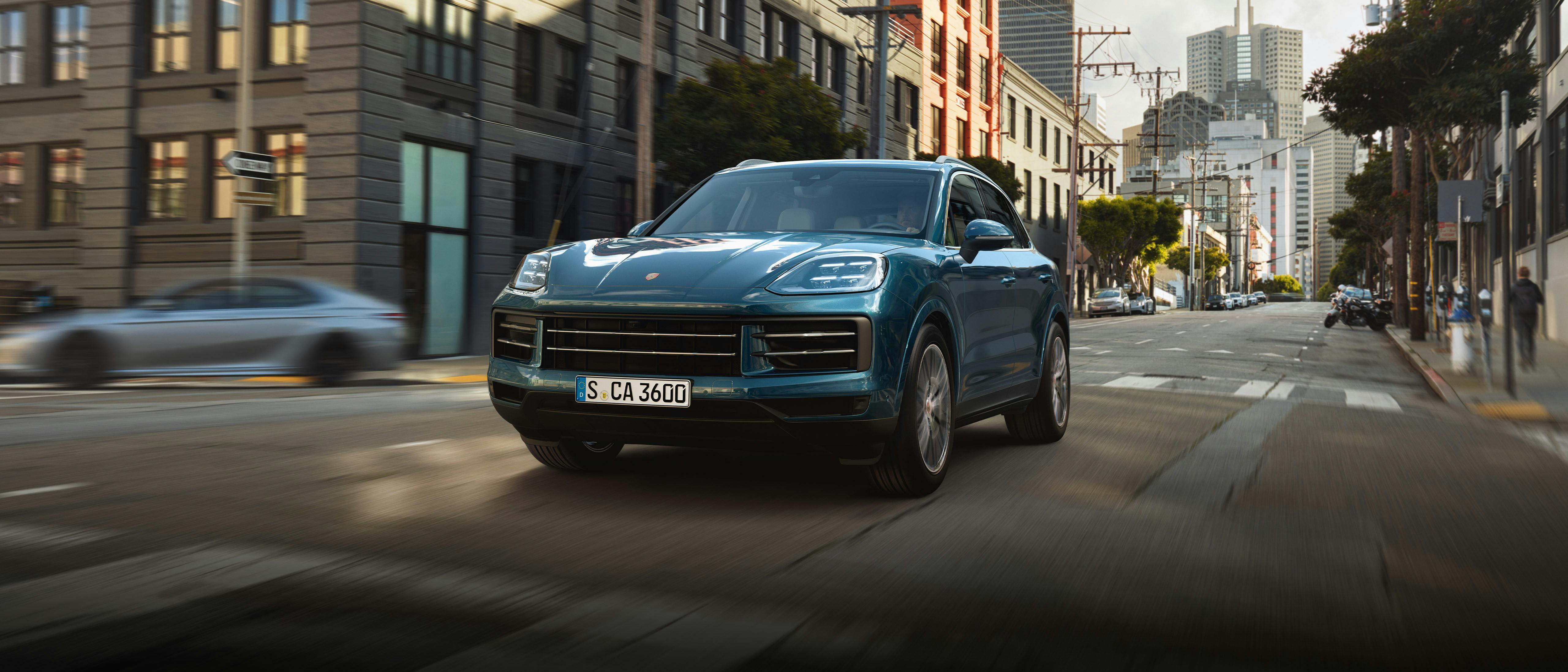 A blue Porsche Cayenne drives through a city street.