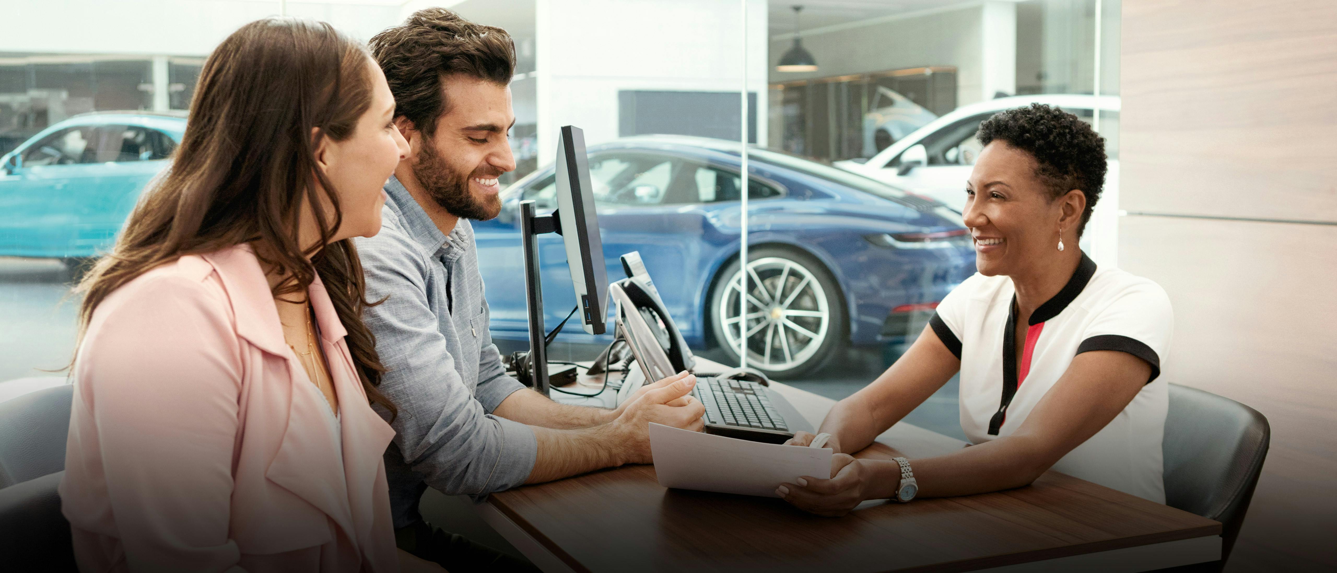 Ein Paar und eine Beraterin lächeln während einer Beratung im Porsche-Autohaus.