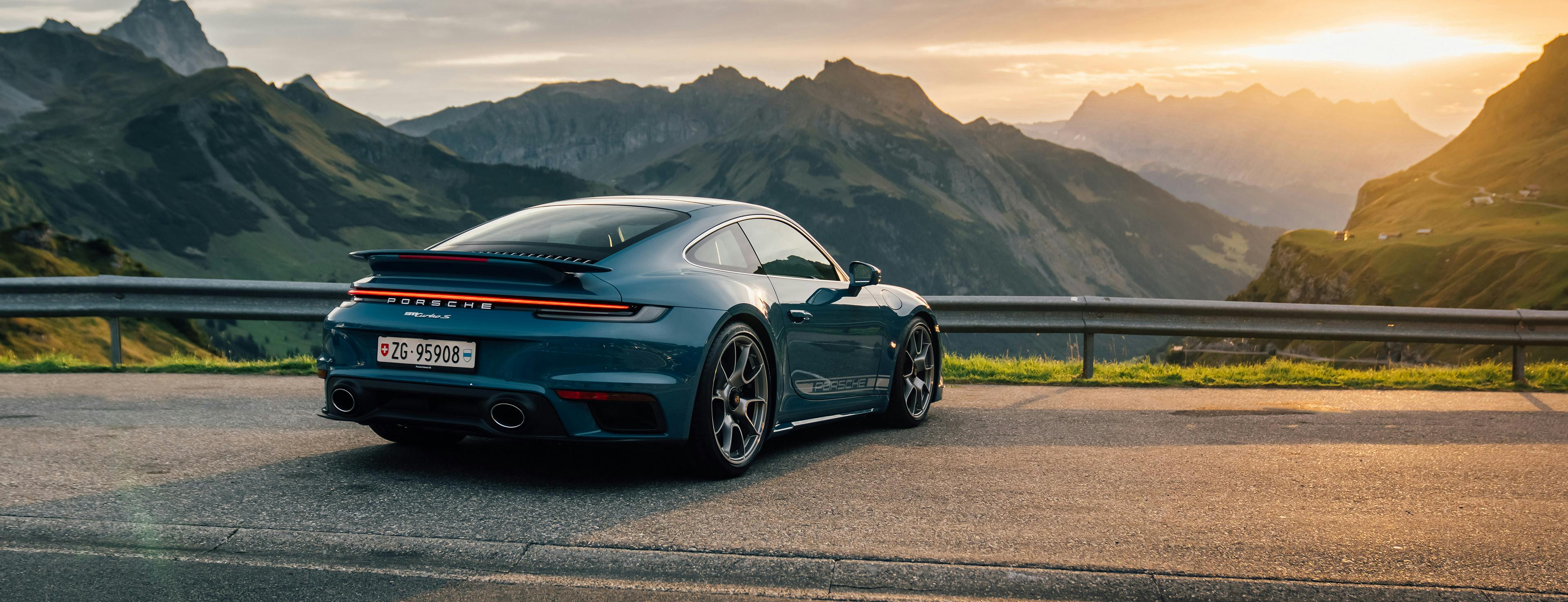 Ein blauer 911 Turbo S steht auf einer Strasse mit dem Heck zum Betrachter, im Hintergrund ist ein Sonnenuntergang zu sehen.