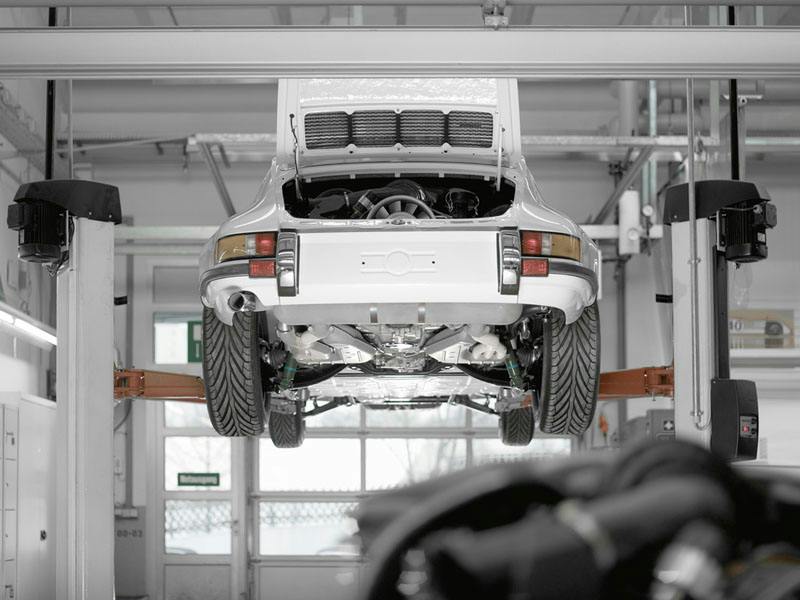 A white Porsche 911 on a lifting platform in a workshop.