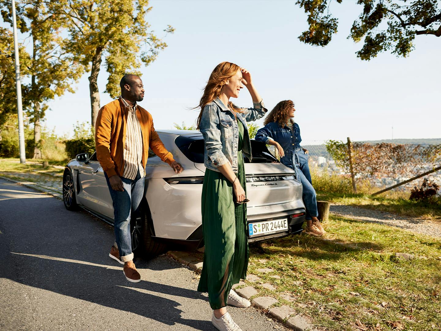 Deux femmes et un homme se tiennent joyeusement près d'un véhicule Porache.