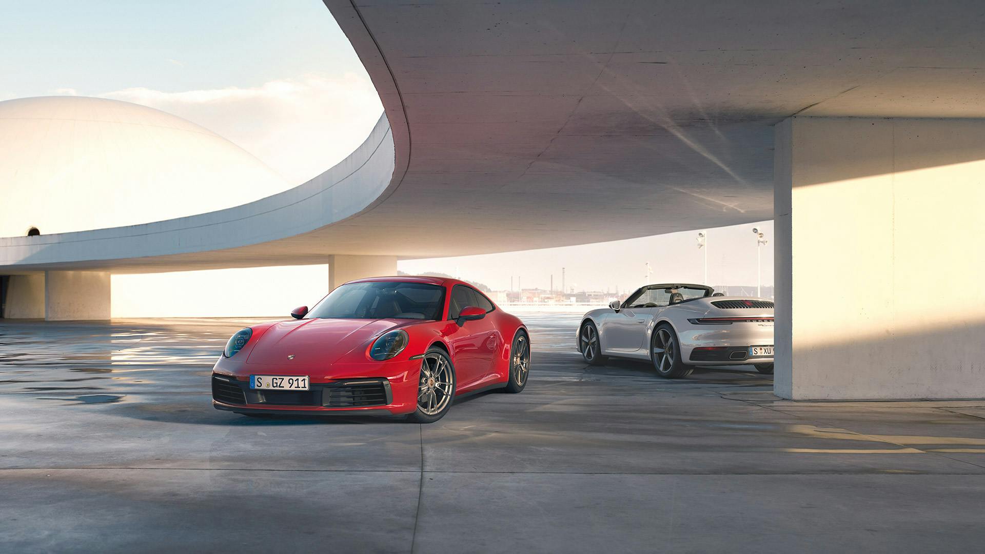 Zwei Porsche 911 Modelle parken unter einer Brücke.