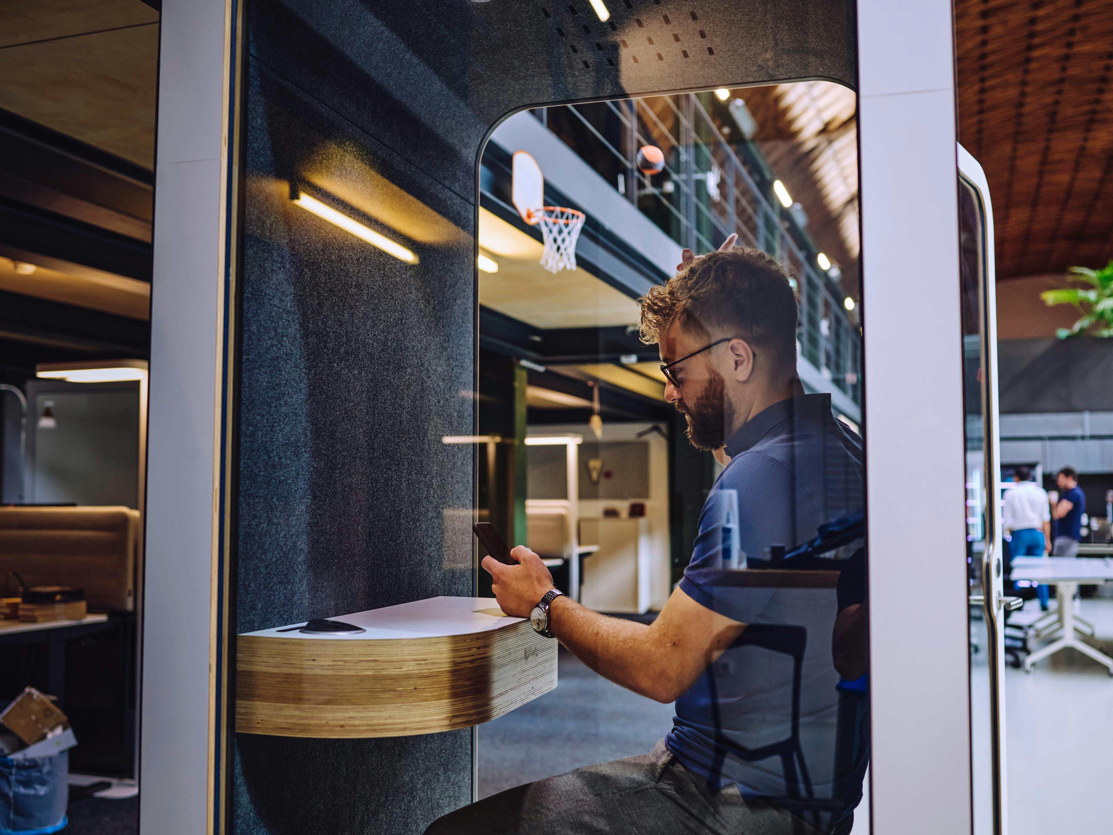 An office at Porsche: a man is sitting in a phone booth, typing intently on his mobile phone.