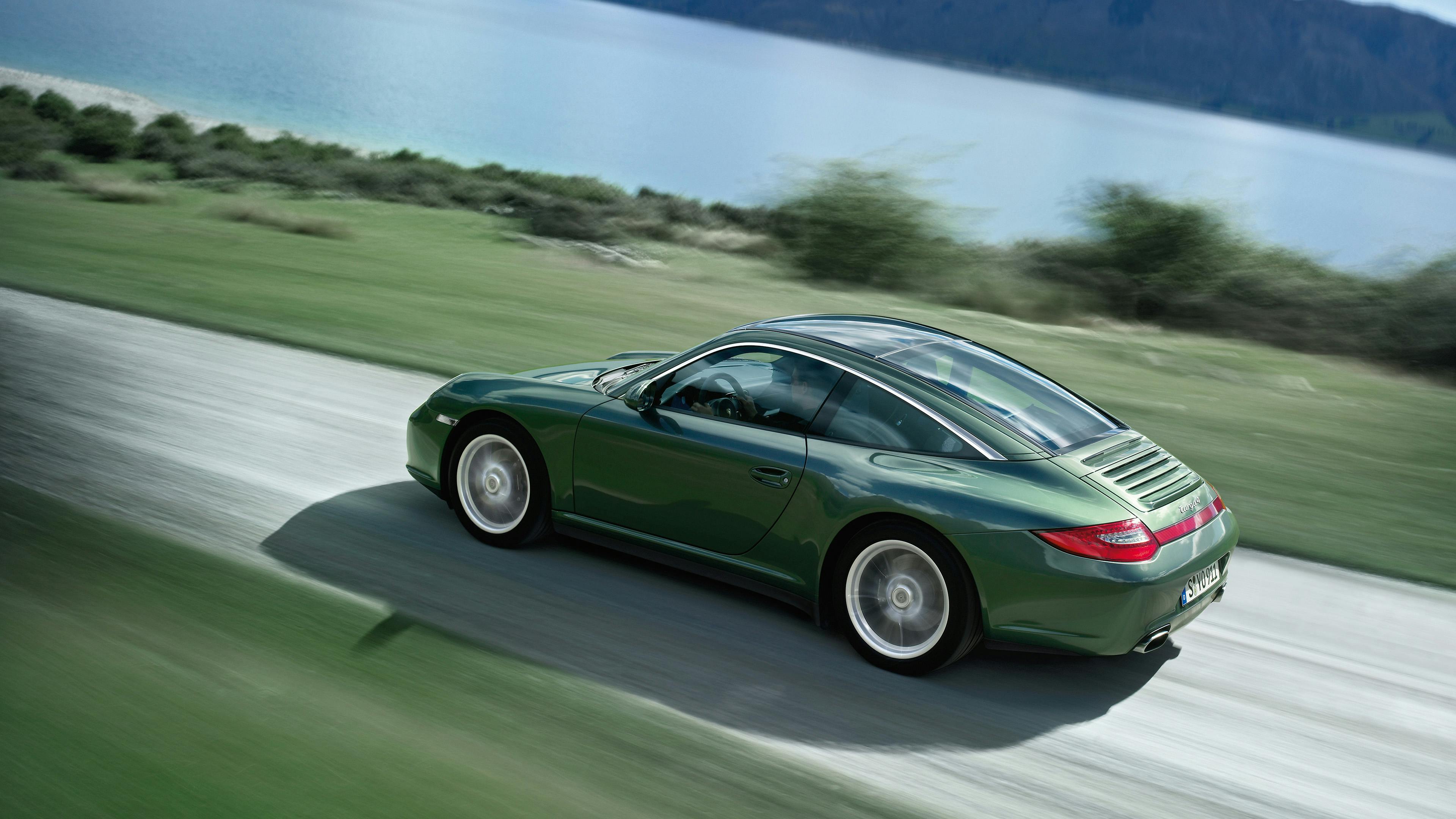 Driving green 911 Targa 4 type 997 on a country road surrounded by green meadow.