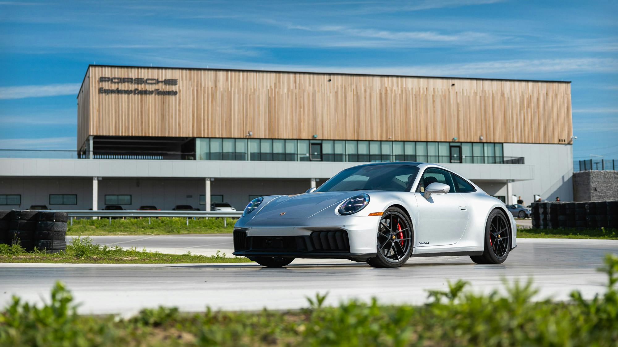Une Porsche 911 argentée sur une piste avec un bâtiment moderne en arrière-plan.