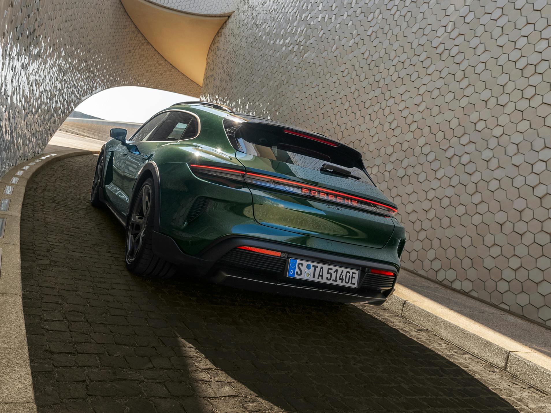 Rear view of a Porsche Taycan Turbo Cross Turismo driving up a steep, winding driveway.