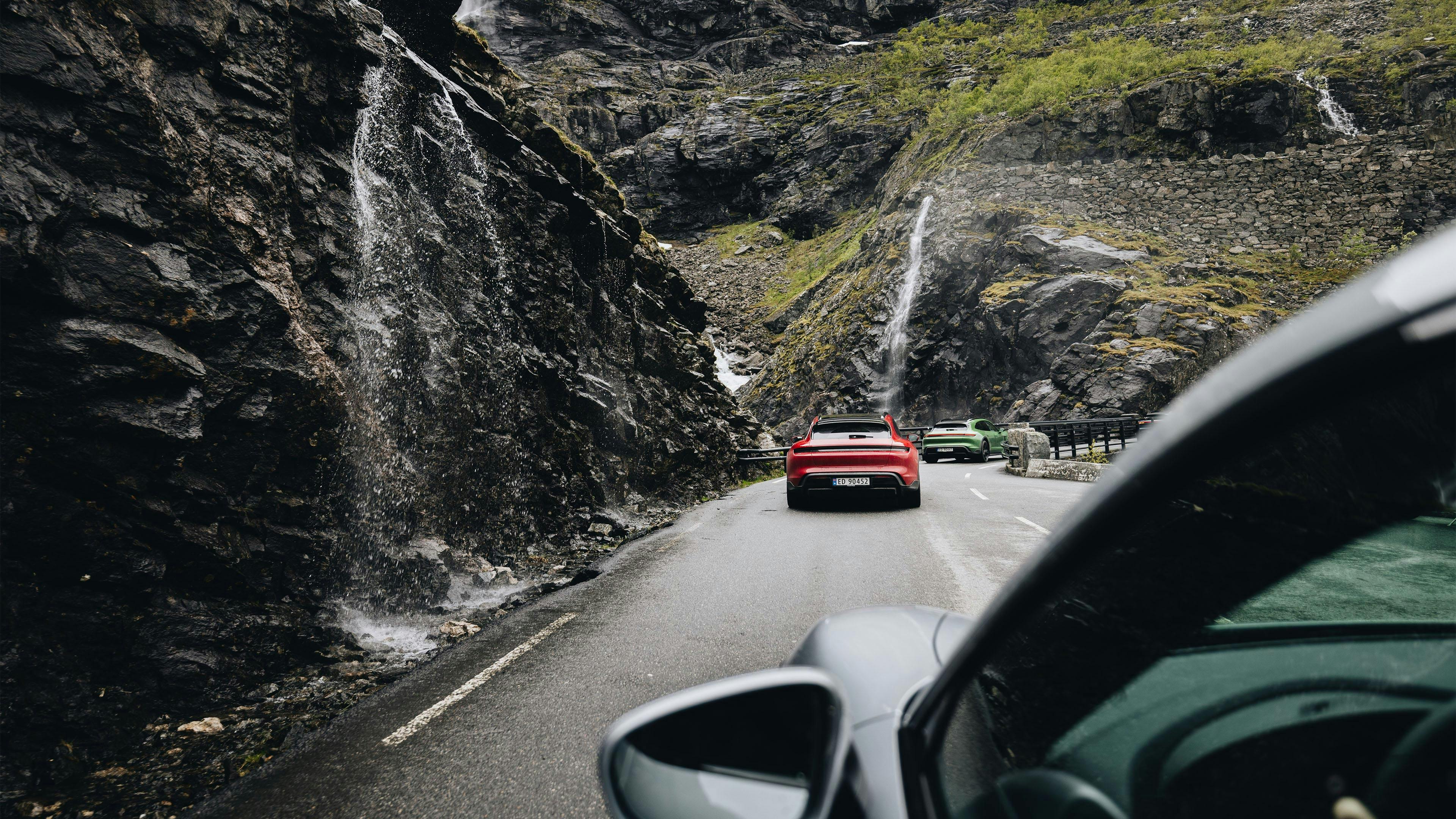 Rodeado de colinas rocosas, un Porsche sigue a otros dos vehículos por la carretera durante Travel Experience Norway.