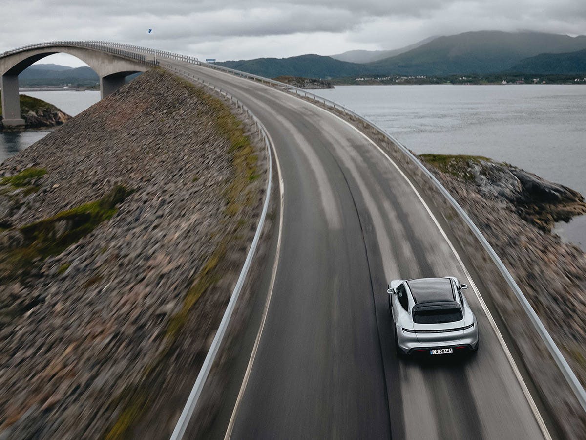 Un vehículo Porsche se acerca a un puente. Al fondo: las montañas y la inmensidad del agua.