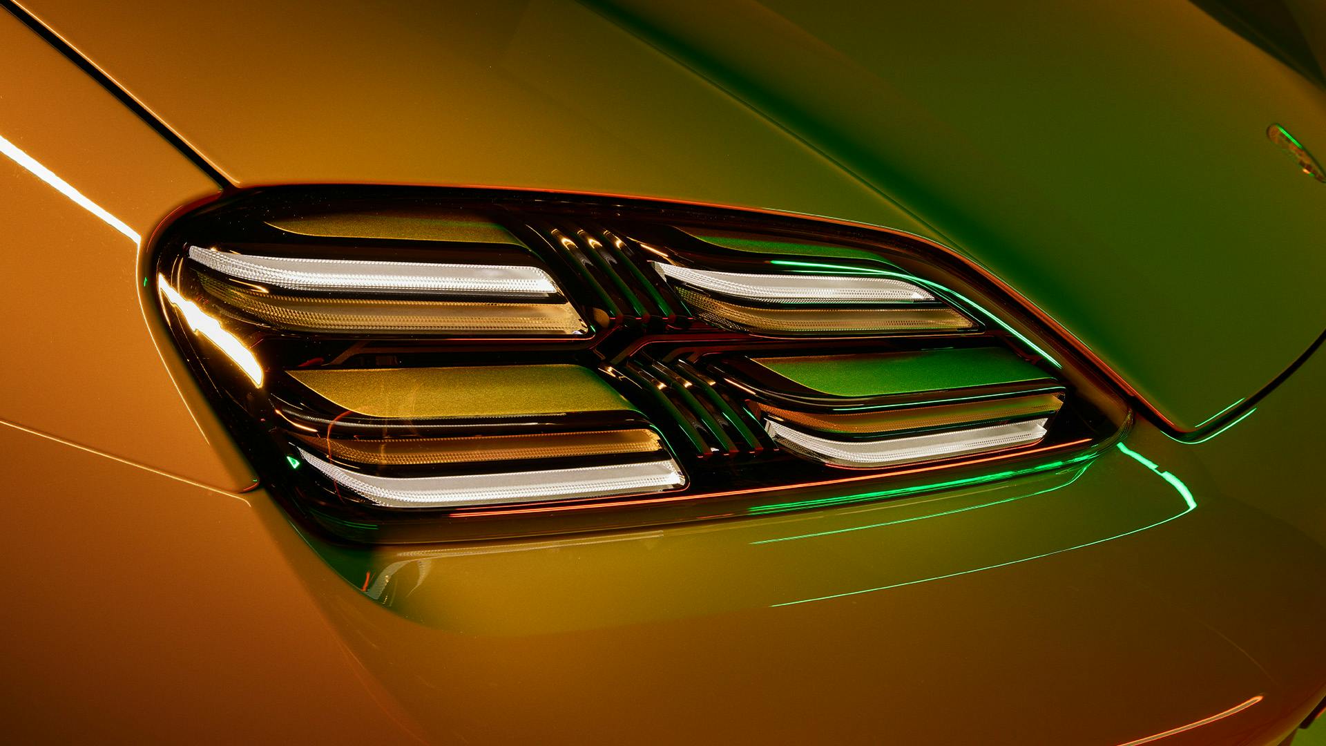 Der Frontscheinwerfer eines Porsche Fahrzeugs in futuristischem orangegrünen Licht.