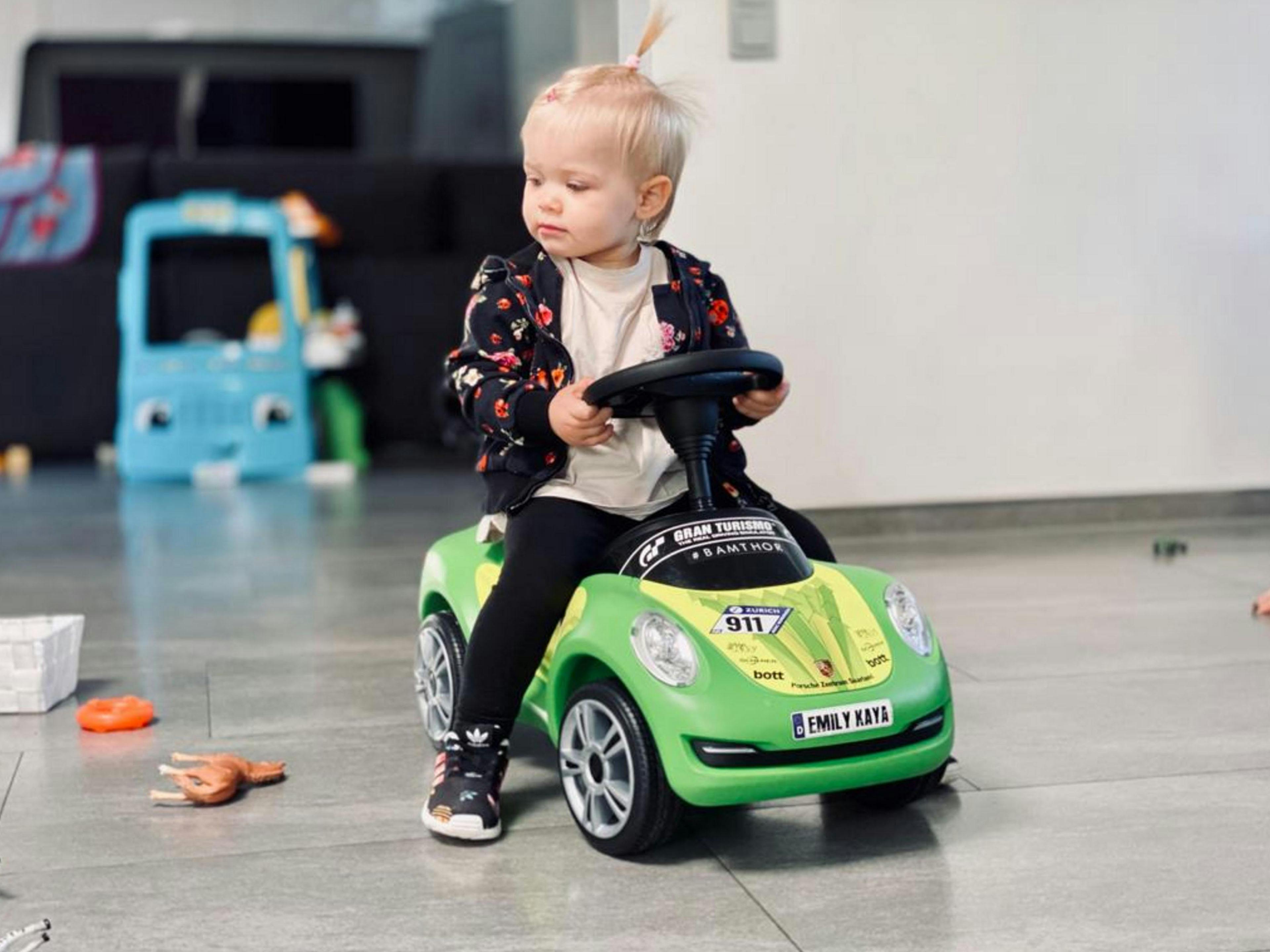 Kleinkind auf dem grünen Rutscheauto Baby Porsche.