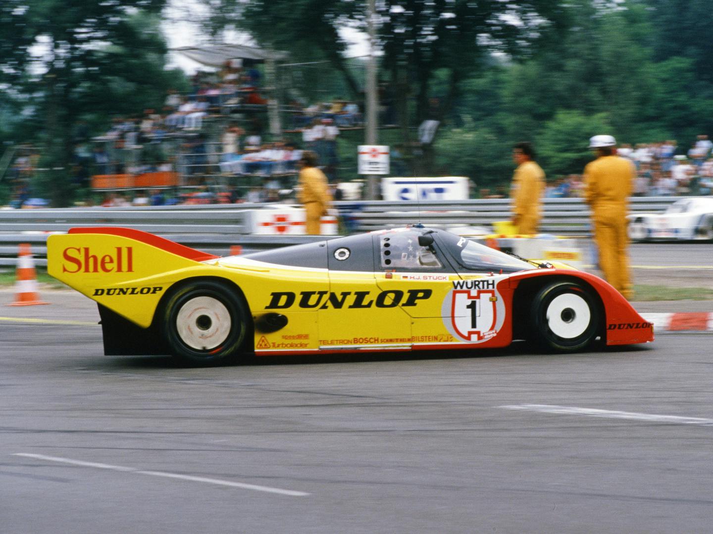 The Shell and Dunlop liveried Porsche 962 endurance race car, number 1, in the pit lane with marshals nearby.
