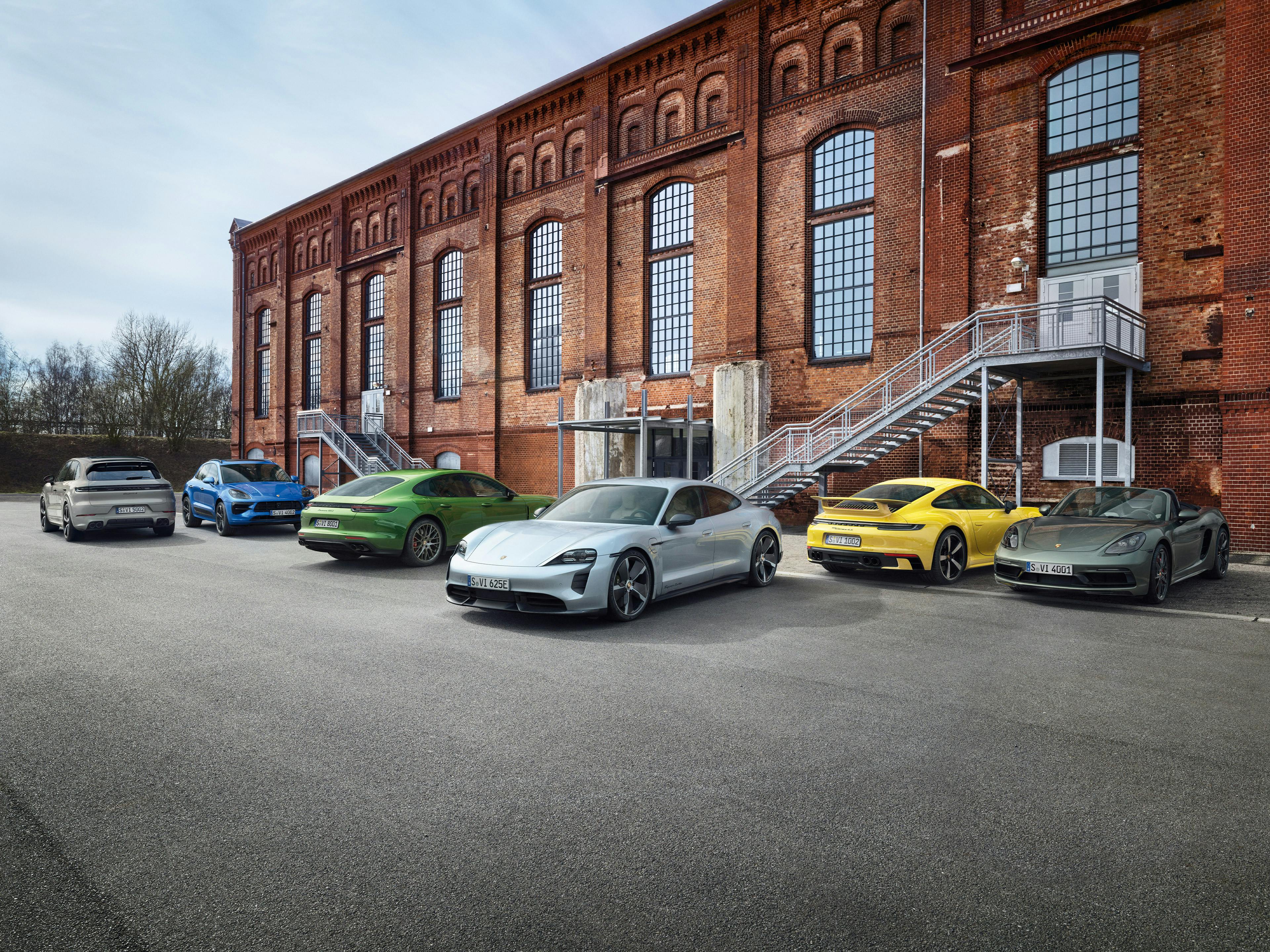 Verschiedene Porsche-Modelle in verschiedenen Farben stehen vor einem Backsteingebäude.