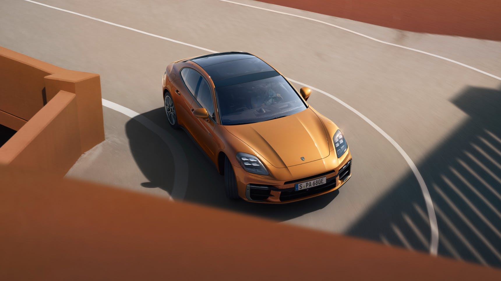 A Porsche Panamera Turbo E-Hybrid in Madeira Gold Metallic is shown driving into a turn.