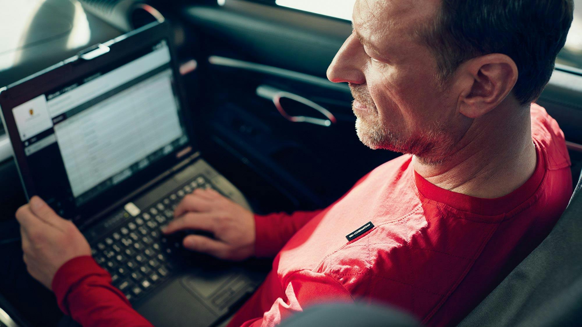 Porsche mechanic checking his laptop inside a vehicle.