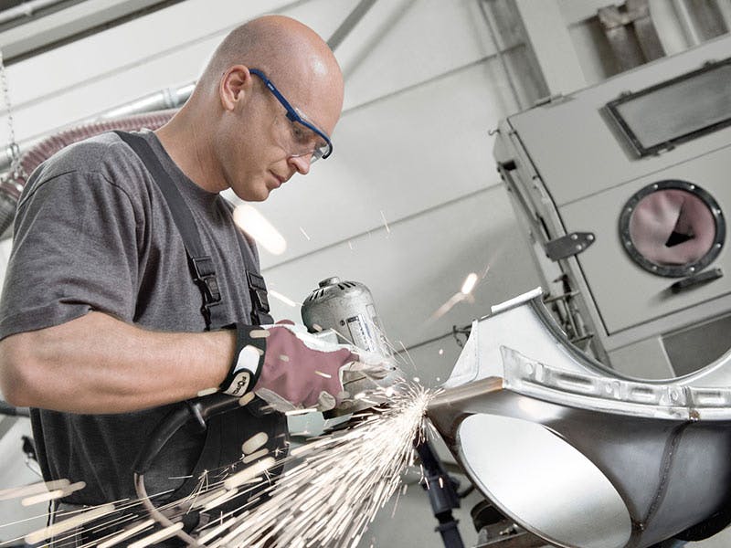 Workshop scene: man cleans a weld seam, sparks