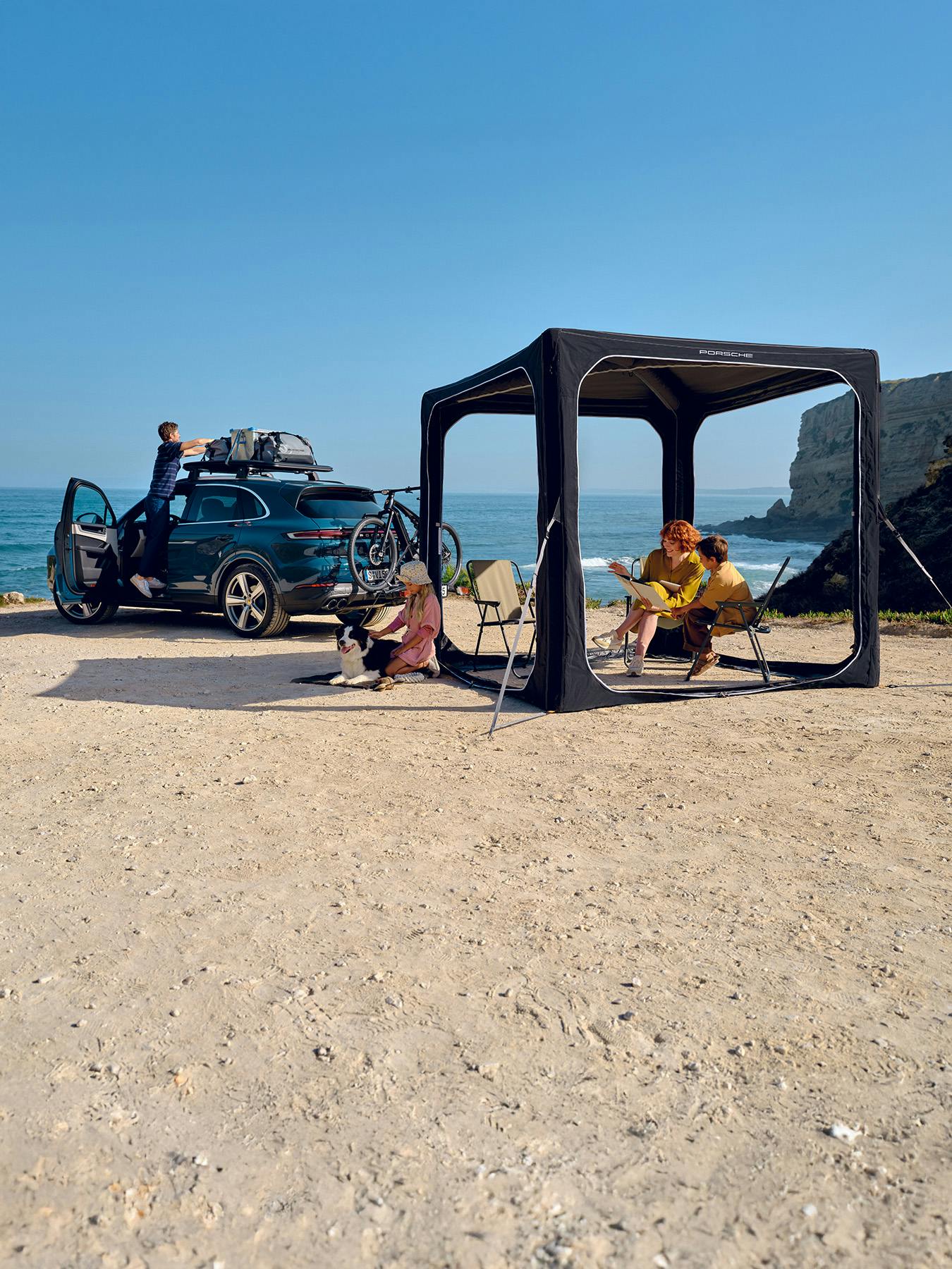 Family camping on the beach with a black pavilion and a Cayenne with a roof rack and rear bike rack.