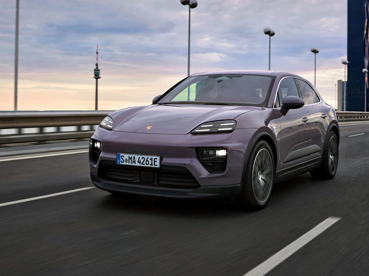 The Macan 4 Electric driving along a dual carriageway with tall office buildings visible in the background.