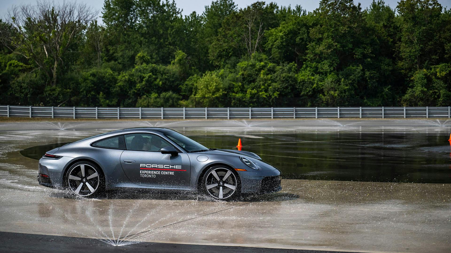 A grey Porsche 911 drifting across a wet circular concrete driving pad.