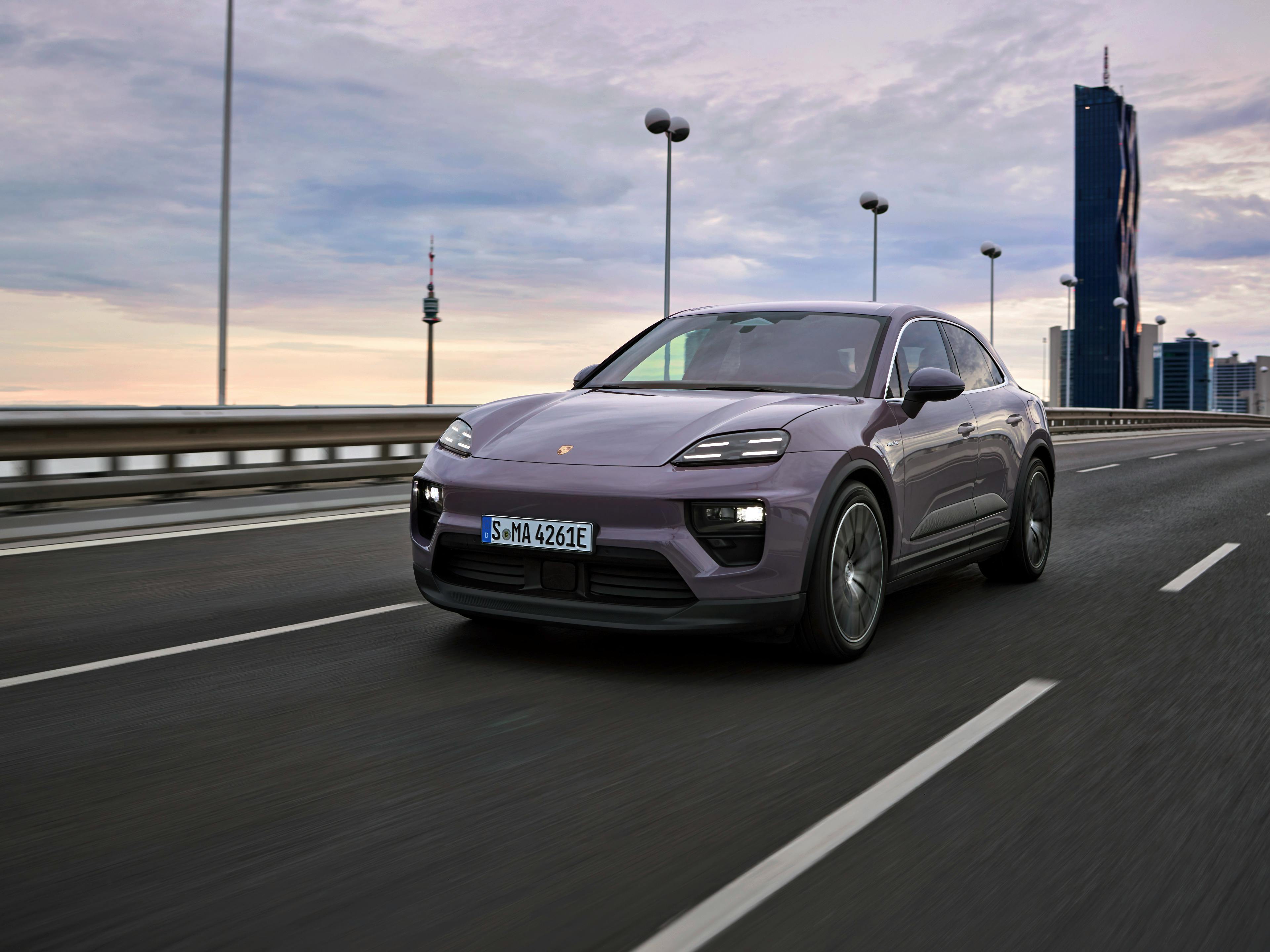 The Macan 4 Electric driving along a dual carriageway with tall office buildings visible in the background.
