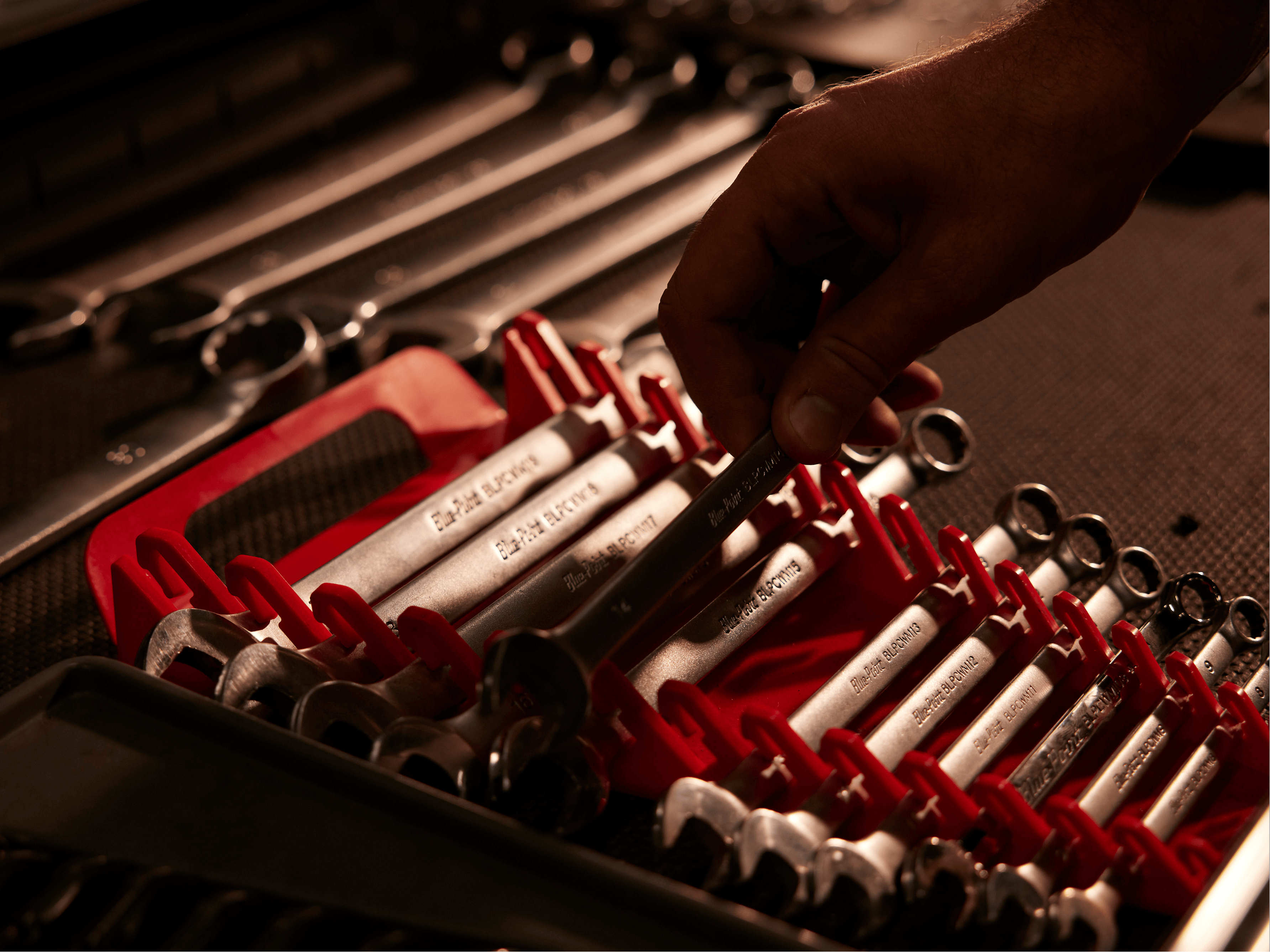 Hand reaches for wrench in red tool organizer with sorted wrenches in Porsche workshop drawer.
