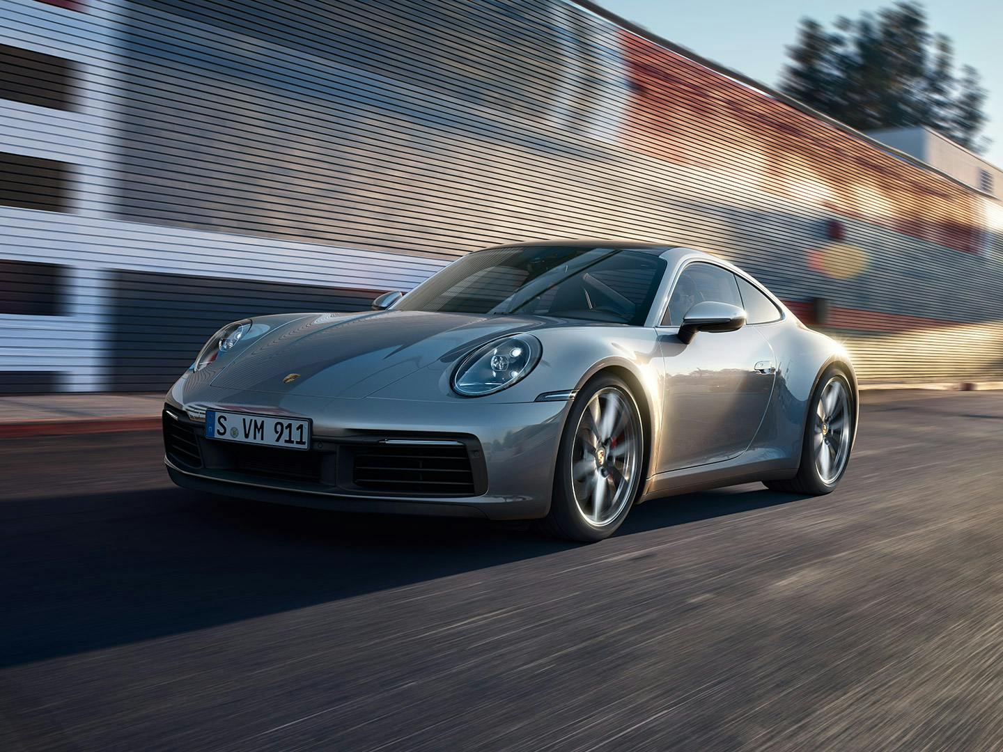 A silver Porsche 911 drives along a road.